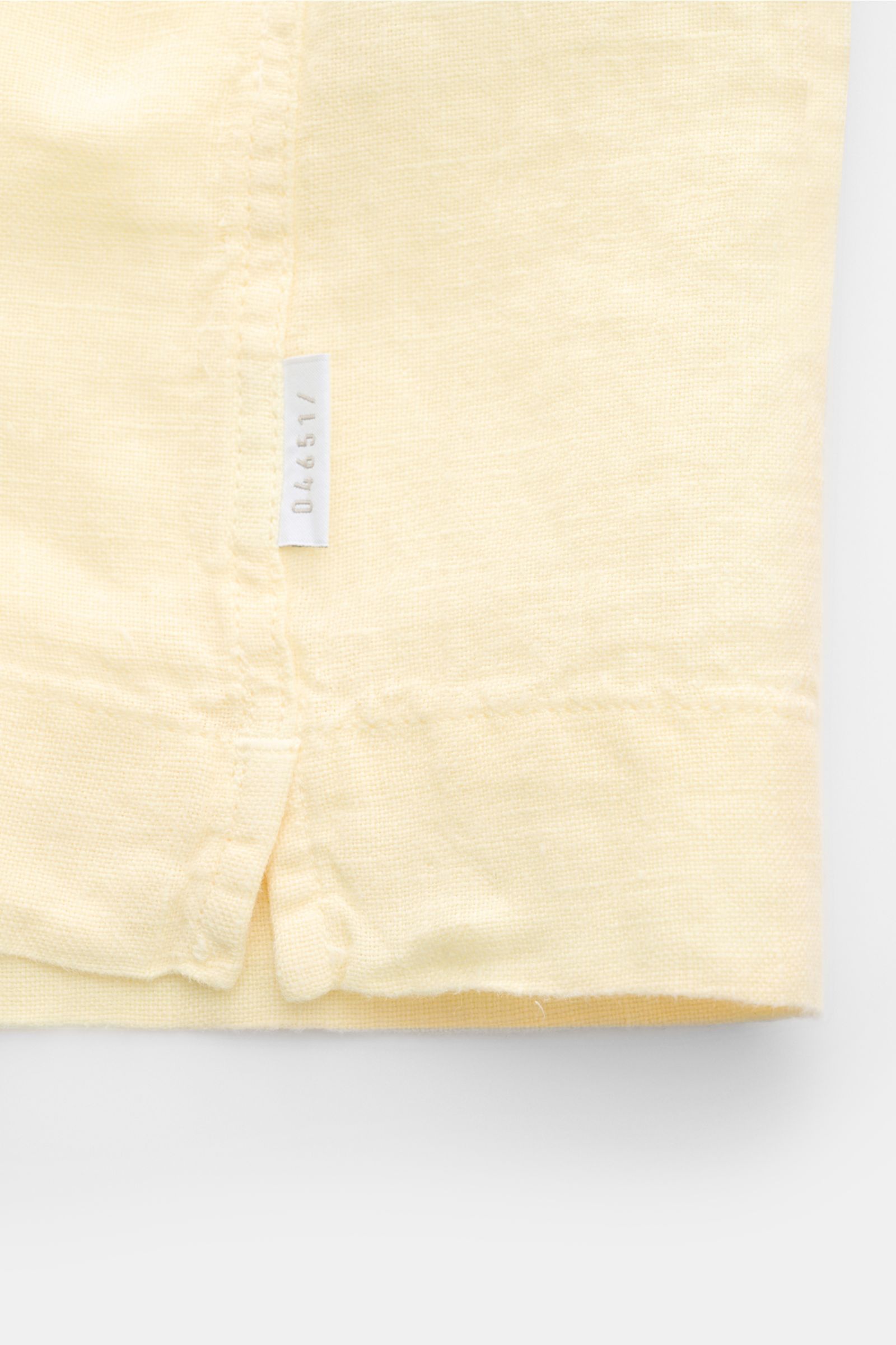 Alt-Tag (124 Zeichen): Nahaufnahme des Saums mit kleinem Weblabel des 04651/ A trip in a bag Leinen-Kurzarmhemd Kubanischer Kragen pastellgelb.