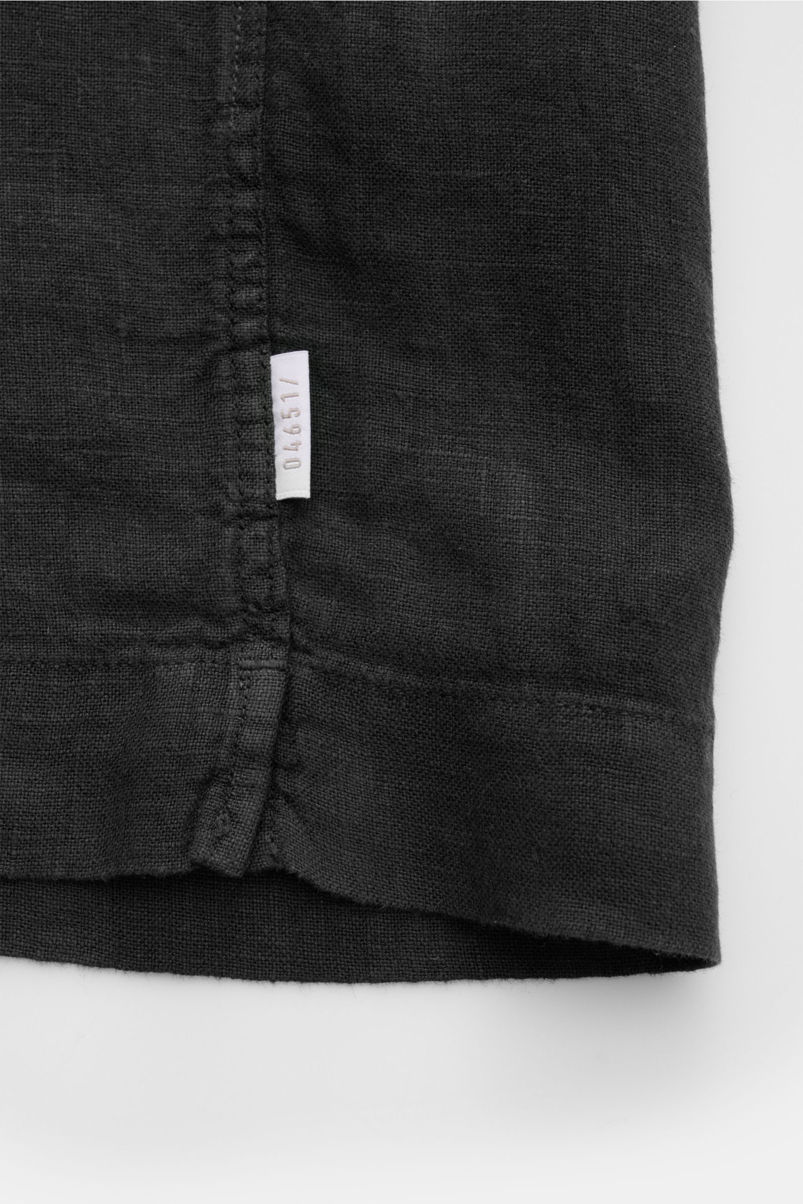 Alt-Tag (124 Zeichen): Detailaufnahme des Saumverlaufs mit kleinem Weblabel des schwarzen 04651/ A trip in a bag Leinen-Kurzarmhemd Kubanischer Kragen.