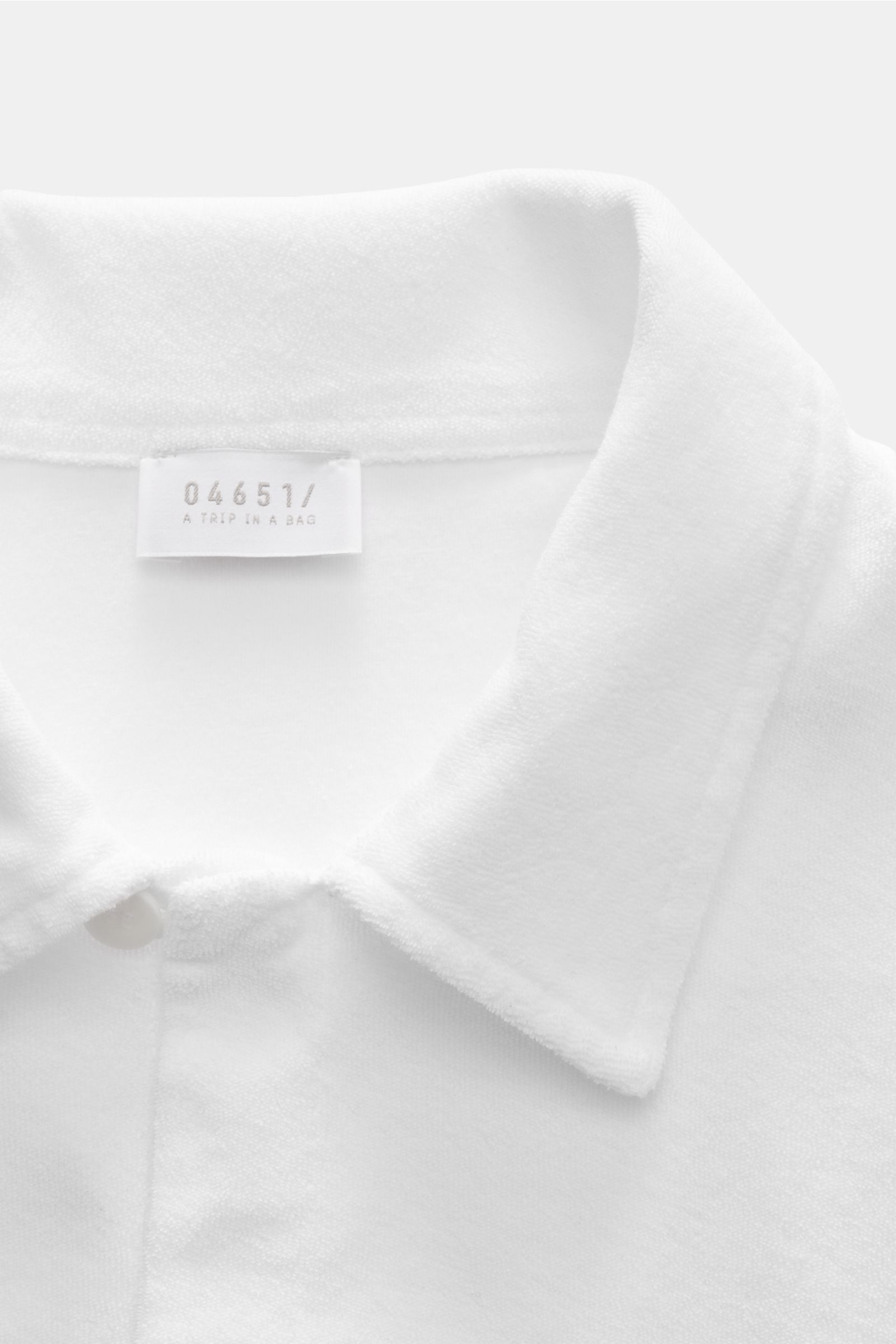Close-up front view of the collar and label of the 04651/ A trip in a bag Frottee-Kurzarmhemd 'Terry Cuba' weiß made of soft pure cotton terry. Urlaubsgefühl zum Anziehen: Das Kurzarmhemd 'Terry Cuba' von 04651/ A TRIP IN A BAG aus angenehmem Baumwoll-Fro