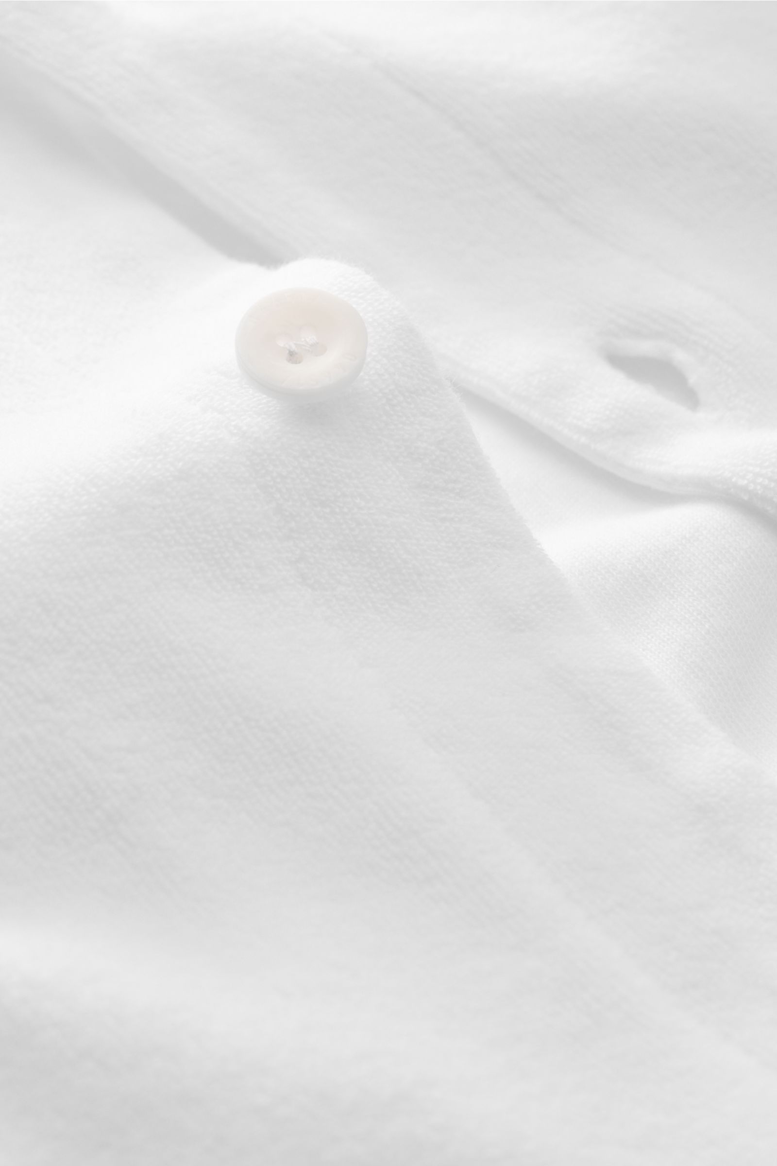 Close-up front view of 04651/ A trip in a bag Frottee-Kurzarmhemd 'Terry Cuba' weiß with white button on soft cotton terry fabric. Urlaubsgefühl zum Anziehen: Das Kurzarmhemd 'Terry Cuba' von 04651/ A TRIP IN A BAG aus angenehmem Baumwoll-Frottee wird nic