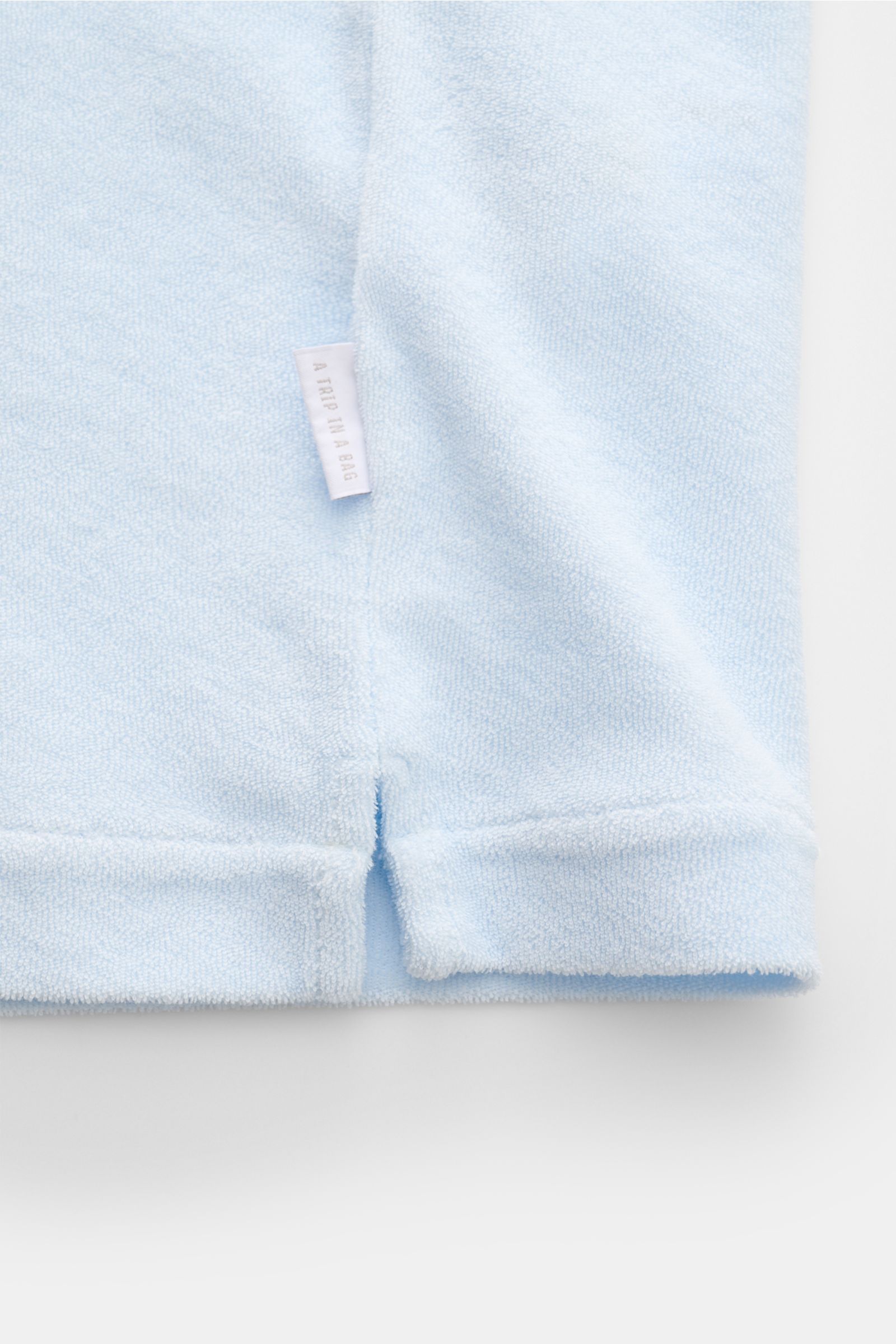 04651/ A trip in a bag Frottee-Kurzarmhemd 'Terry Cuba' pastellblau in Nahaufnahme der Saumkante mit kurzem Schlitz und kleinem Weblabel aus weichem Baumwoll-Frottee.