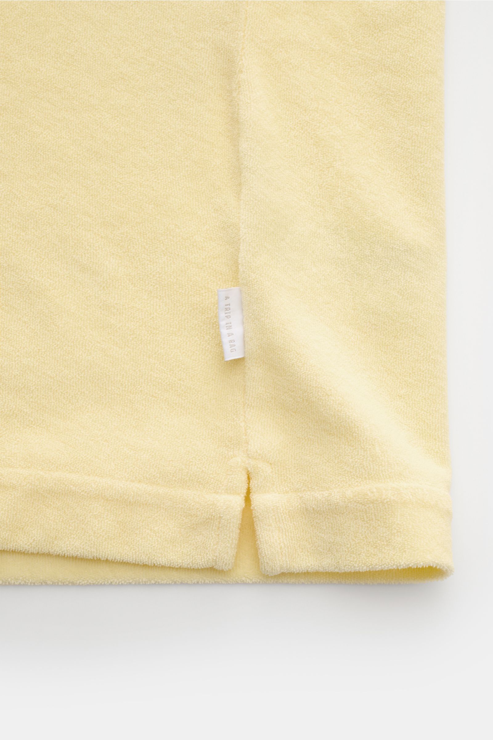 04651/ A trip in a bag Frottee-Kurzarmhemd 'Terry Cuba' pastellgelb, Detailaufnahme Saum mit kurzem Schlitz und kleinem Weblabel, Baumwoll-Frottee.