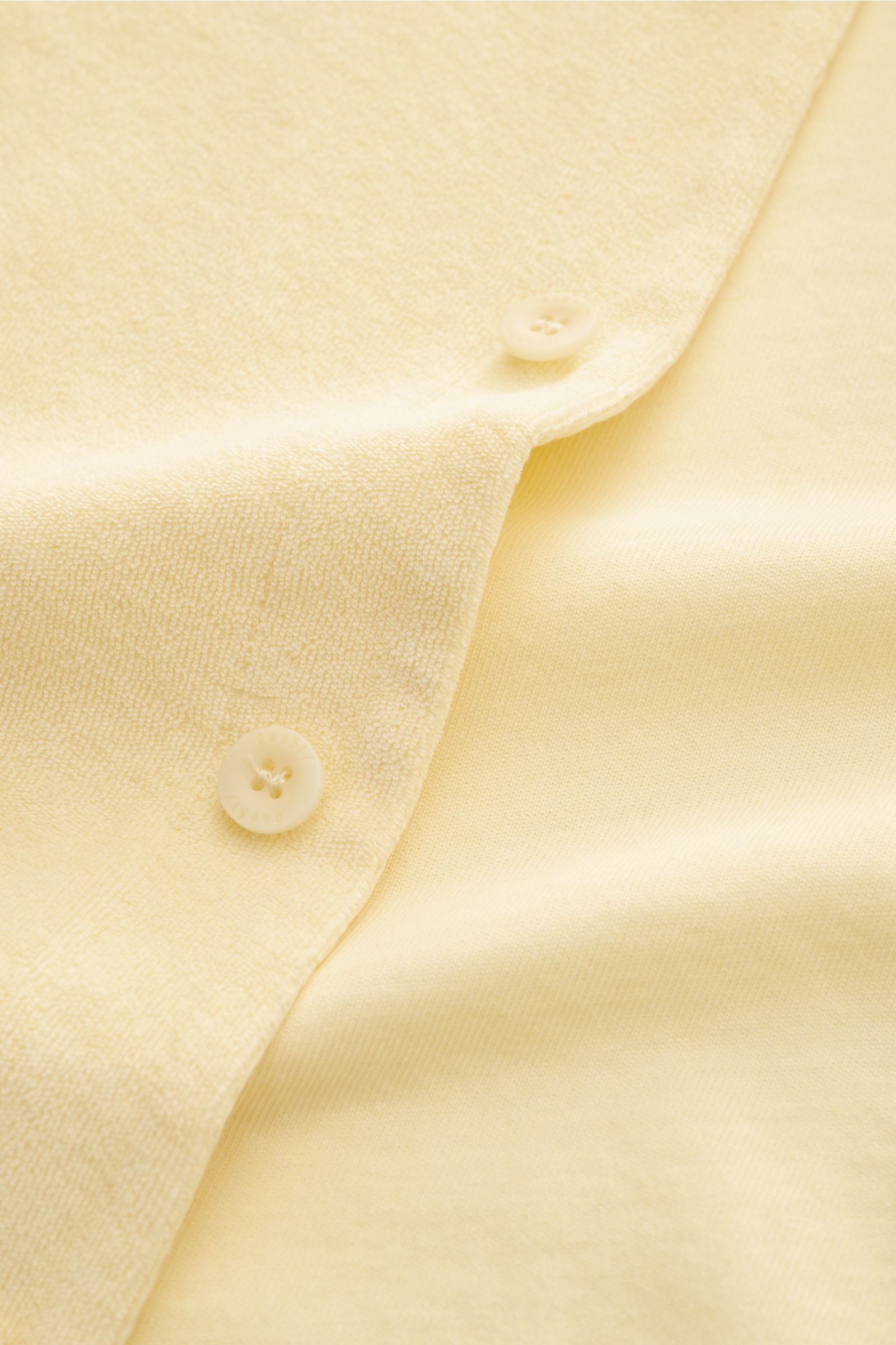 Nahaufnahme des pastellgelben 04651/ A trip in a bag Frottee-Kurzarmhemd 'Terry Cuba' aus Baumwoll-Frottee mit Knöpfen und Saumschlitz.