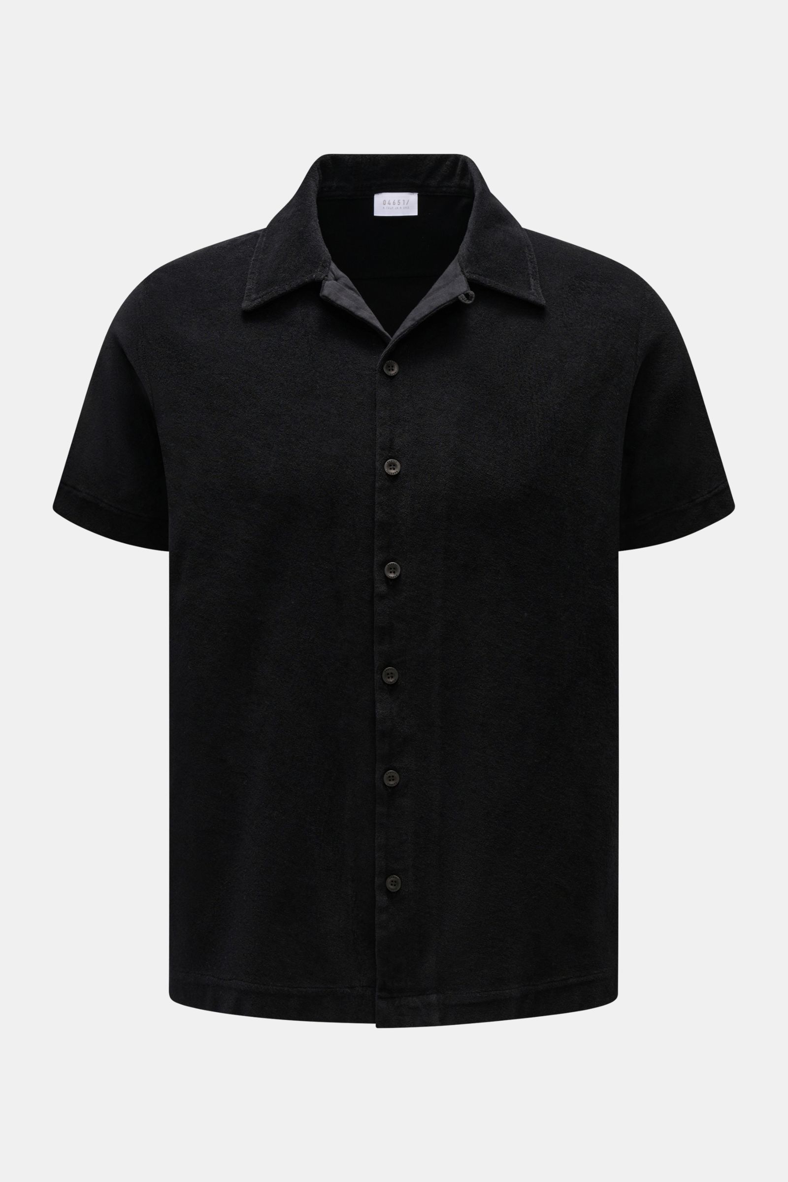 Front view of the 04651/ A trip in a bag Frottee-Kurzarmhemd 'Terry Cuba' schwarz, a black short-sleeve shirt made of soft cotton terry fabric with a regular fit, variable Cuban collar, French button placket, small side seam label, and short hem slits. Ur
