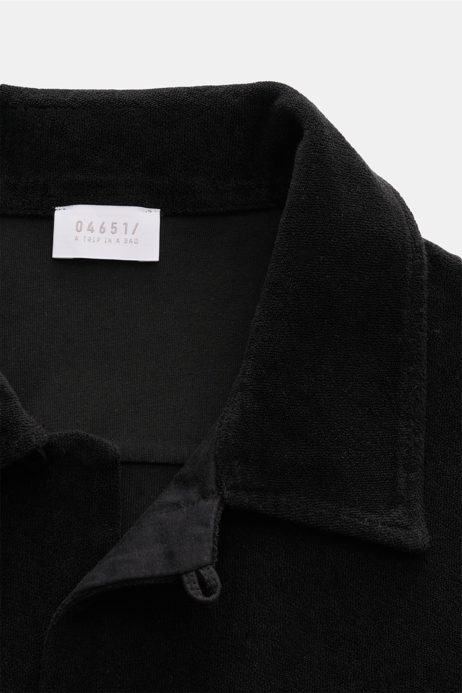 Close-up view of the collar and neckline of the 04651/ A trip in a bag Frottee-Kurzarmhemd 'Terry Cuba' schwarz, showing the soft cotton terry fabric and label. Urlaubsgefühl zum Anziehen: Das Kurzarmhemd 'Terry Cuba' von 04651/ A TRIP IN A BAG aus angene
