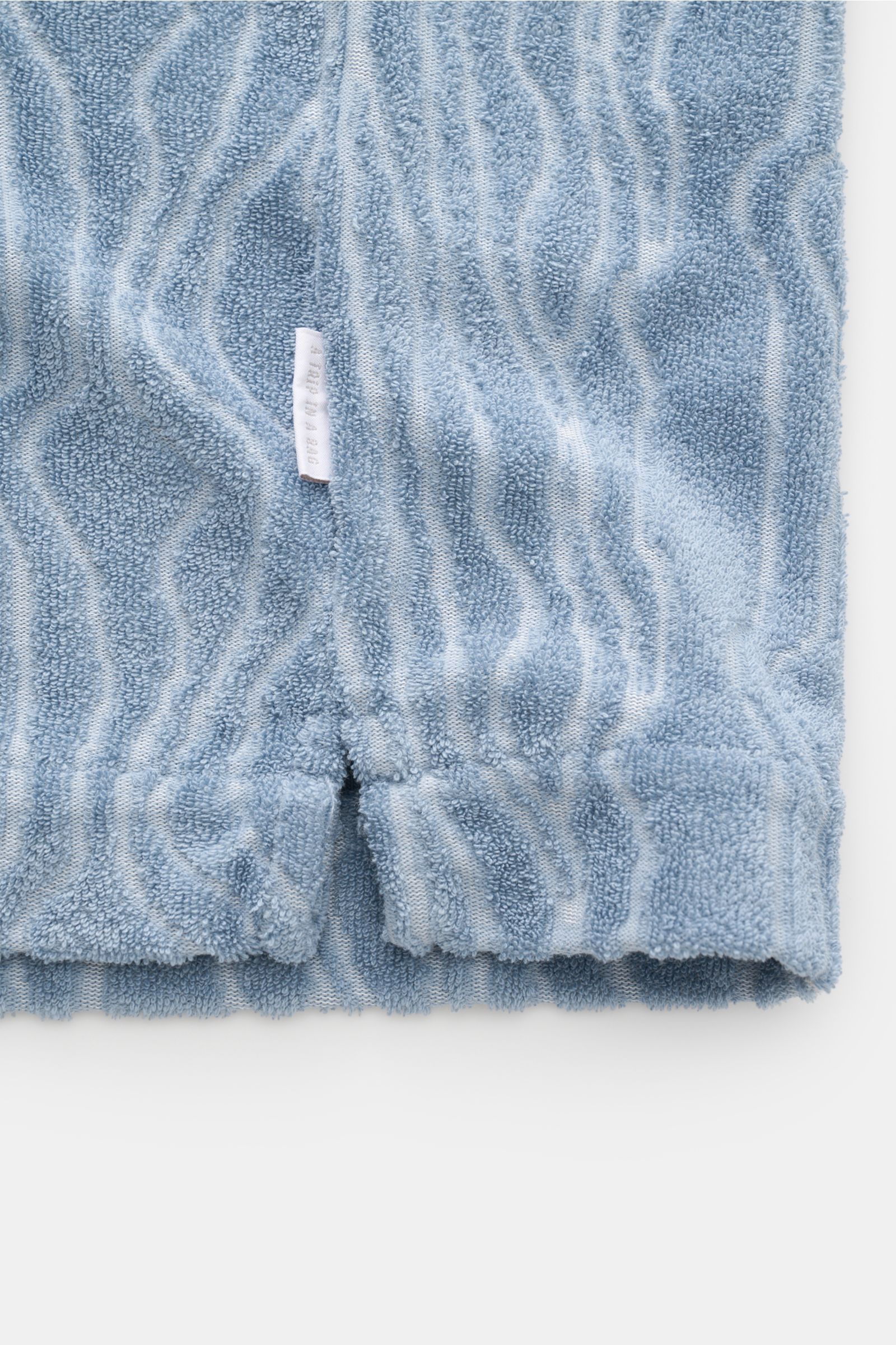 04651/ A trip in a bag Frottee-Kurzarmhemd 'Terry Superkilen' rauchblau, Detailaufnahme des Saums mit kurzem Schlitz und kleinem Weblabel, weicher Baumwoll-Microfaser-Mix.