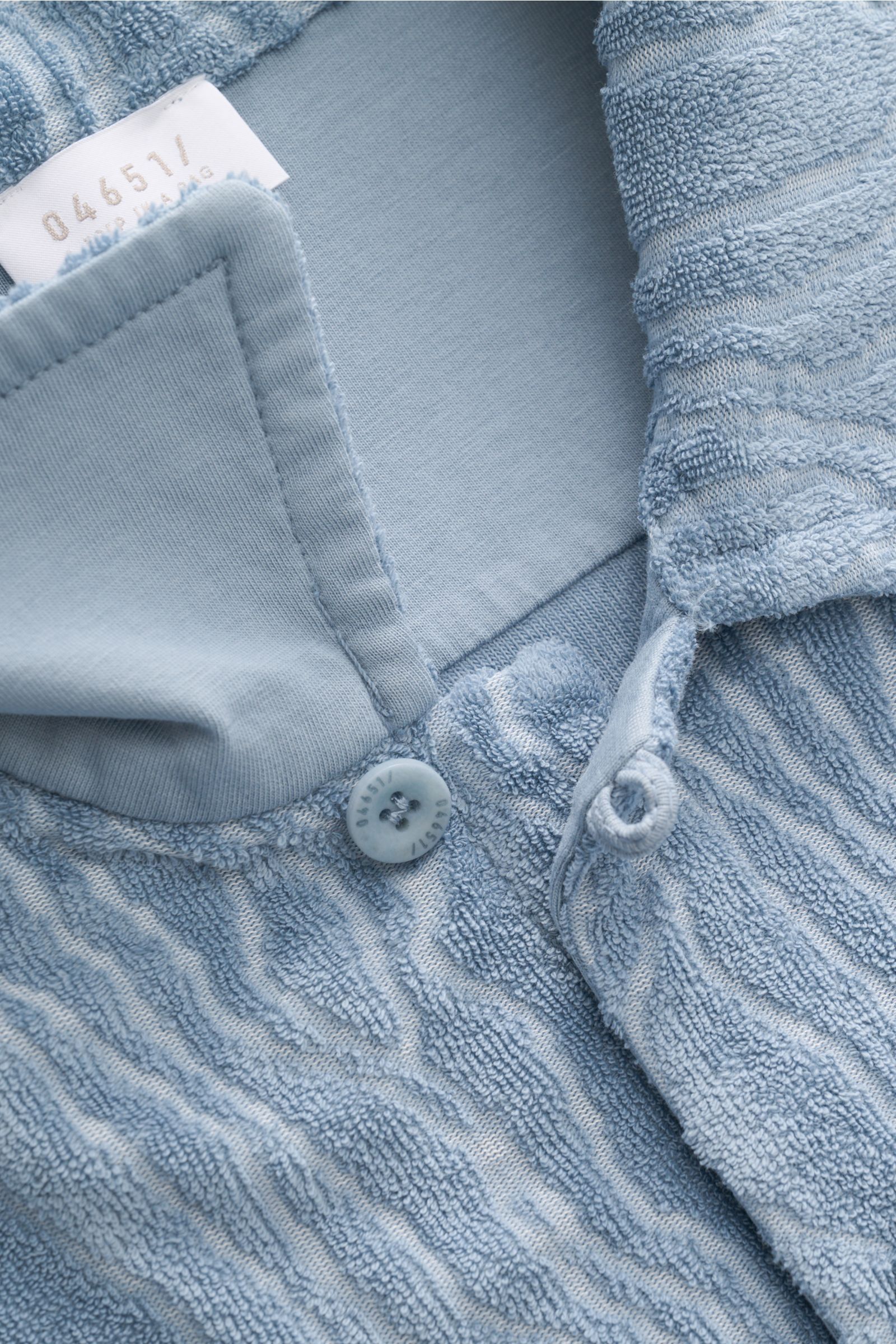 Nahaufnahme aus schräger Perspektive des 04651/ A trip in a bag Frottee-Kurzarmhemd 'Terry Superkilen' rauchblau mit kubanischem Kragen, weichem Griff, französischer Knopfleiste und Allover-Muster inspiriert vom Kopenhagener Superkilen Park.