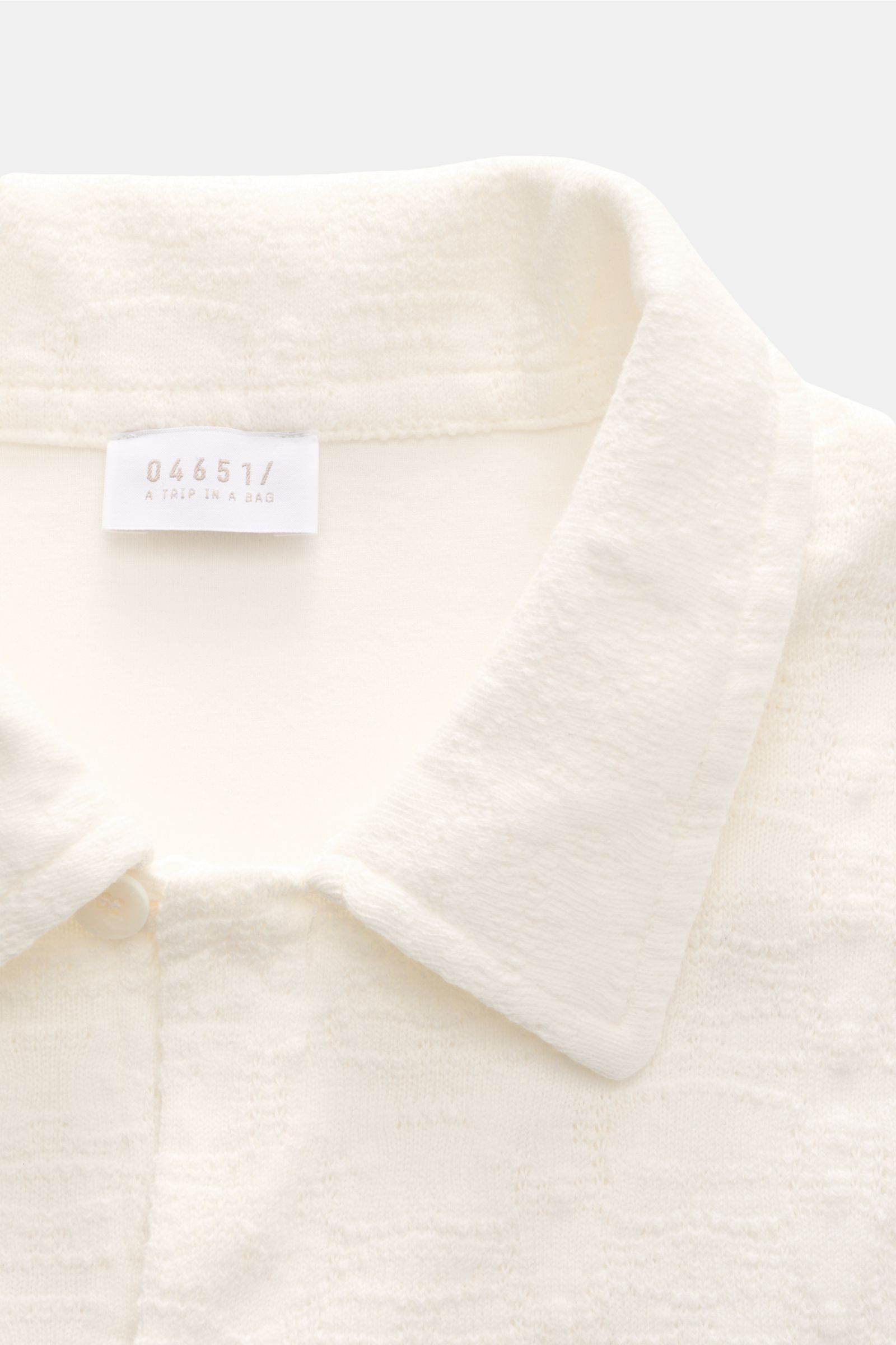 Close-up, top-down view of the collar and label of the 04651/ A trip in a bag Jersey-Kurzarmhemd 'Abstract' Kubanischer Kragen creme, made of pure cotton with a soft touch, breathable jersey fabric featuring a subtle structure pattern, regular fit, variab