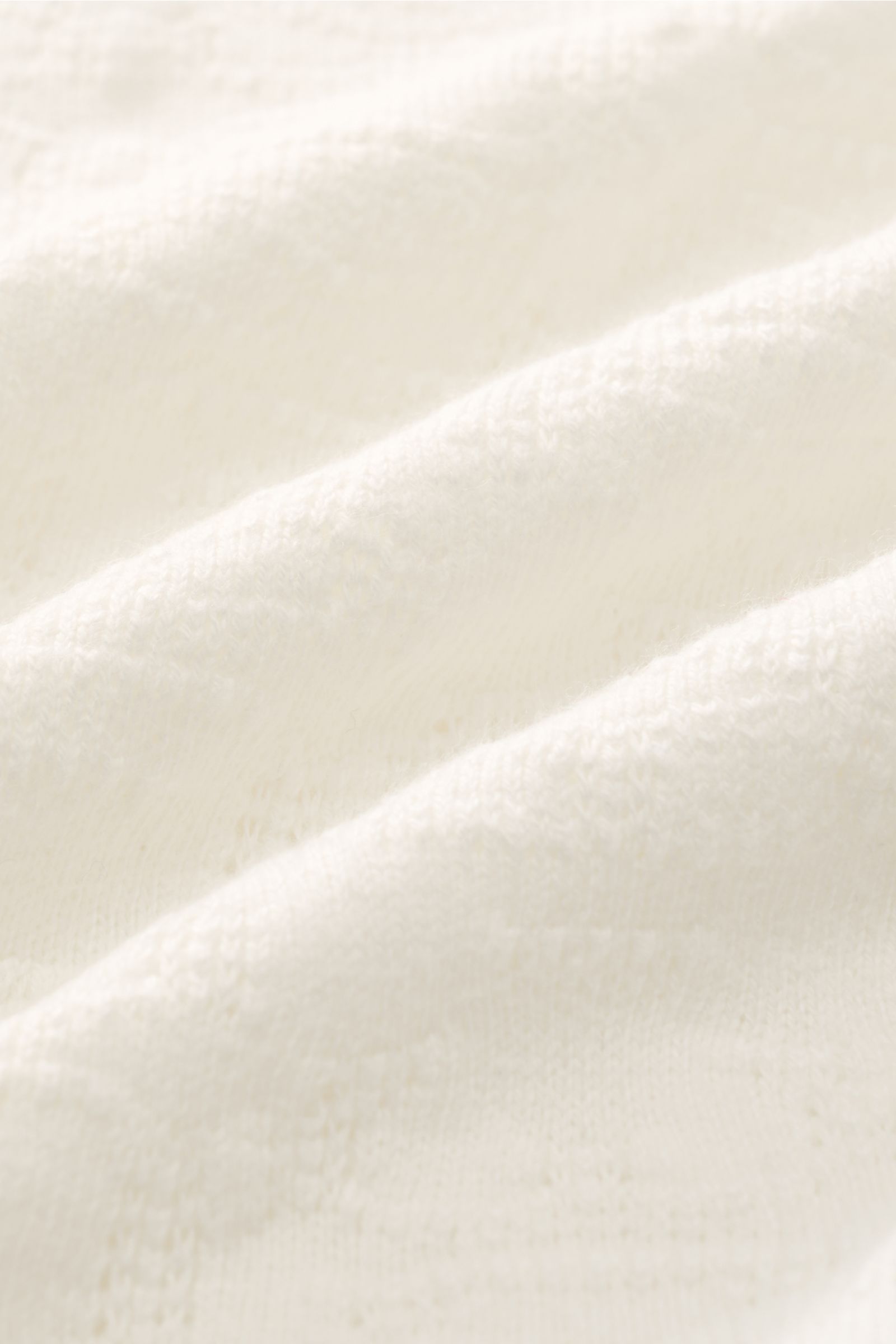 Close-up of soft cream-colored fabric with a subtle textured pattern, showing the material detail of 04651/ A trip in a bag Jersey-Kurzarmhemd 'Abstract' Kubanischer Kragen creme from a top front angle, highlighting its breathable cotton and comfortable j