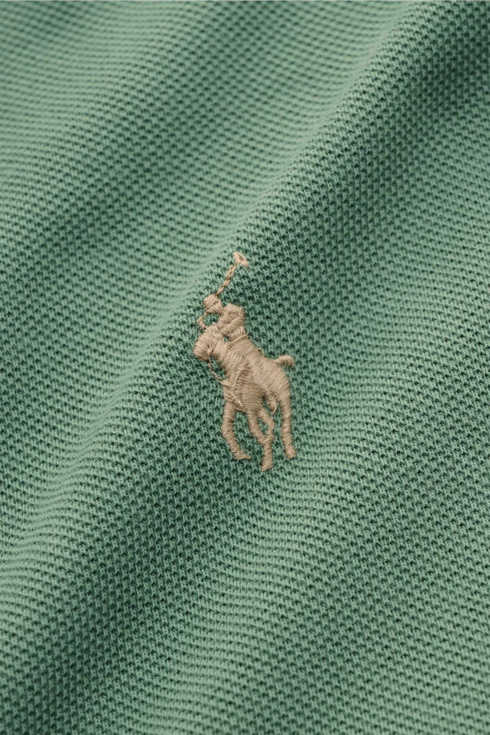Nahaufnahme aus schräger Perspektive eines grünen Polo Ralph Lauren Poloshirts, das ikonische Poloreiter-Stitching auf feinem Piqué-Baumwolljersey zeigt.
