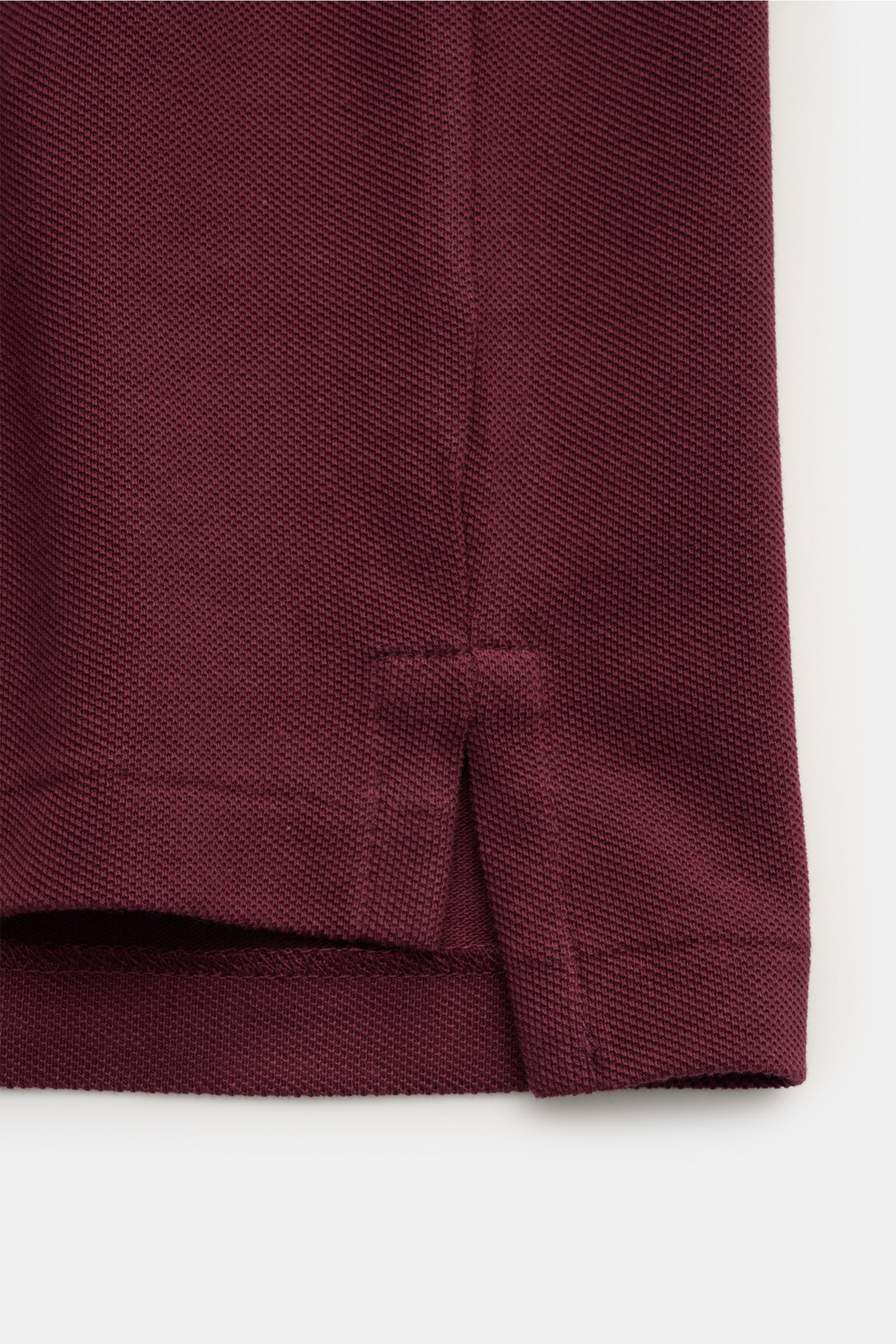 Nahaufnahme der Saumkante eines Polo Ralph Lauren Poloshirt bordeaux aus reiner Baumwolle mit feiner Piqué-Struktur, seitlichem Saumschlitz und leicht verlängerter Rückseite.