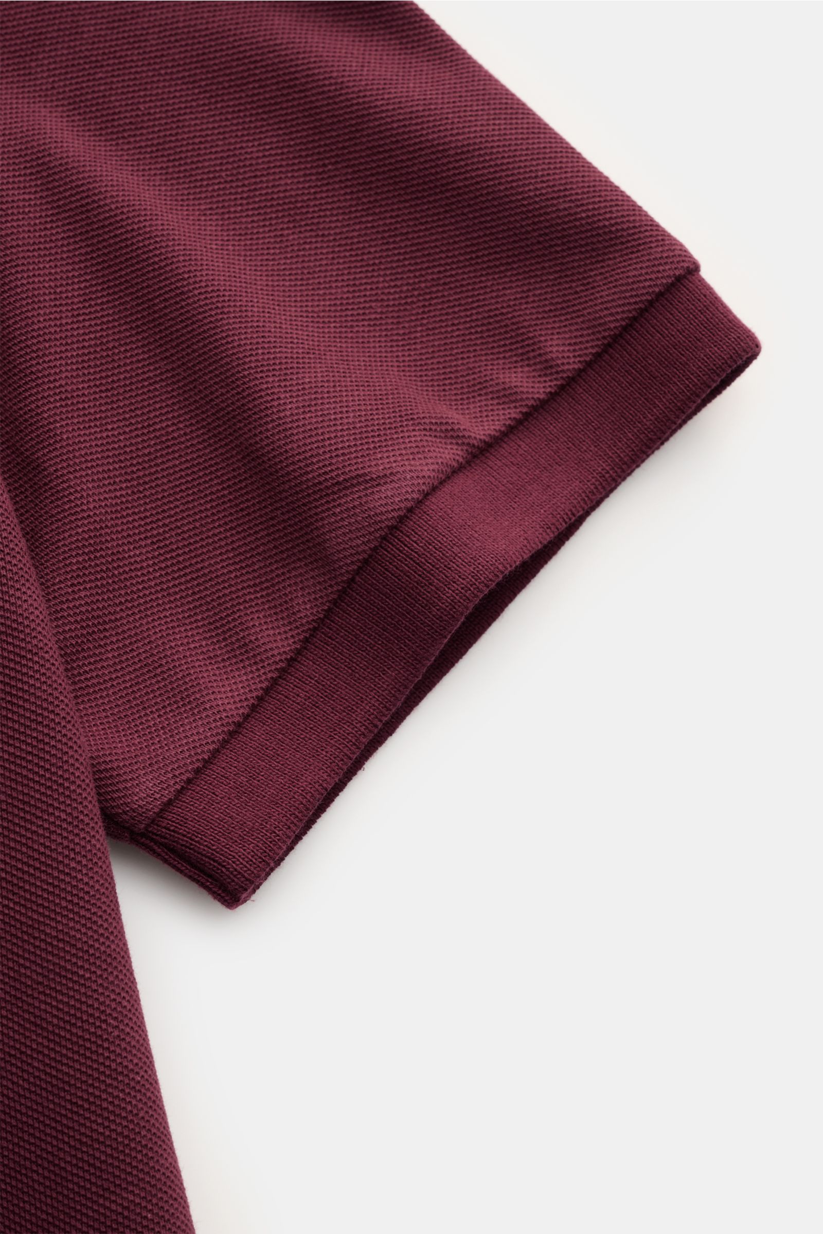 Nahaufnahme des Polo Ralph Lauren Poloshirts bordeaux, Detail der elastischen Ärmelbündchen und feinen Piqué-Struktur aus reiner Baumwolle.