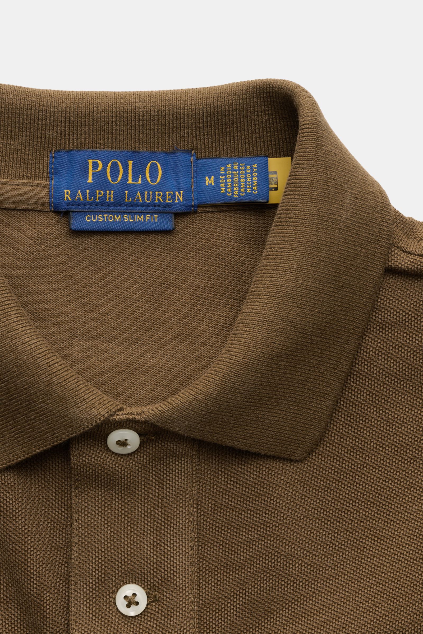 Nahaufnahme des Polo Ralph Lauren Poloshirts braun von oben, zeigt den typischen Polokragen, Zwei-Knopf-Leiste und feine Piqué-Struktur. Seit 1972 der Klassiker aus reiner Baumwolle mit Slim Fit, elastischen Ärmelbündchen, seitlichen Saumschlitzen und iko
