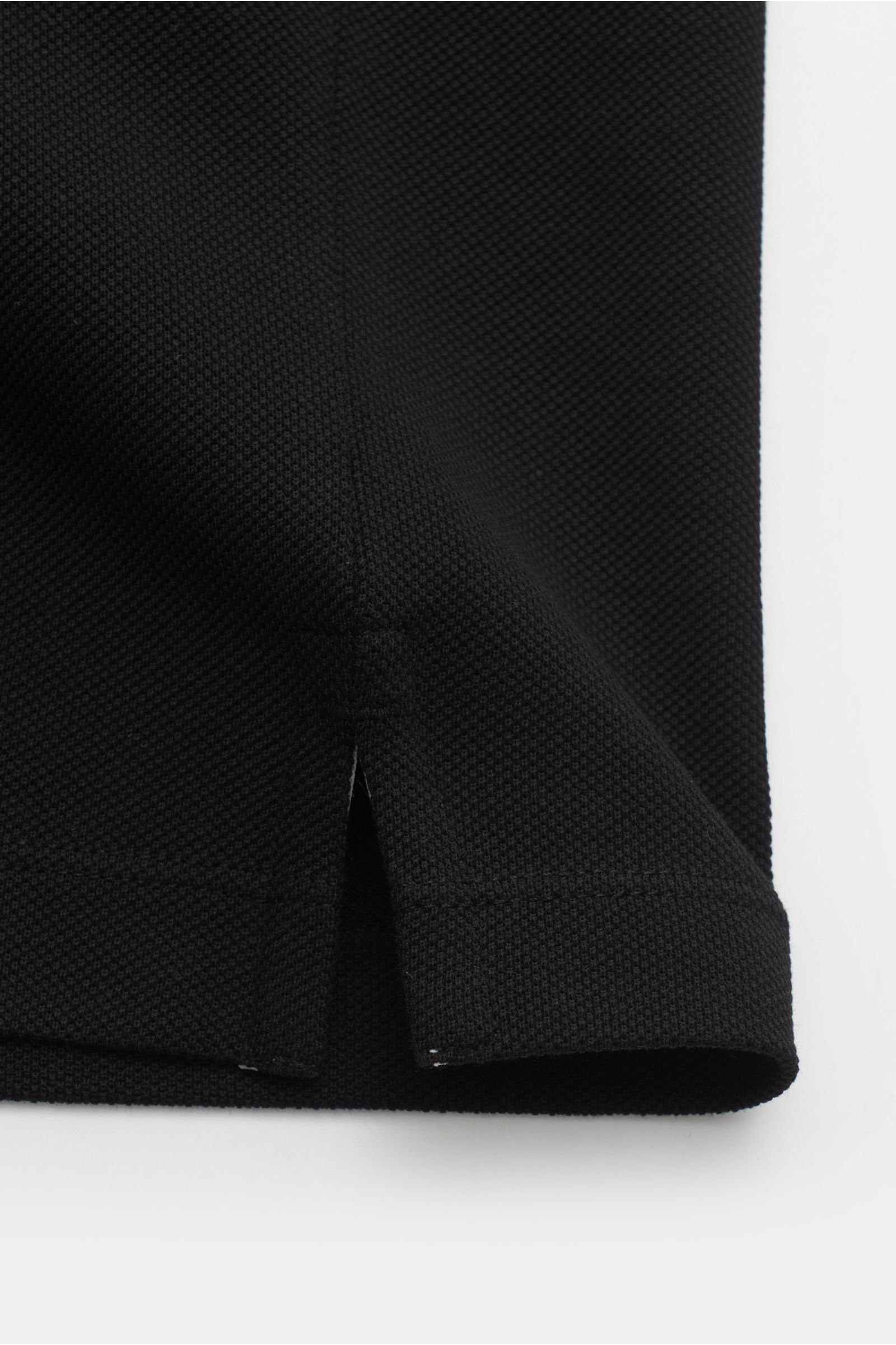 Close-up side detail of the Stone Island Poloshirt schwarz showing the textured cotton piqué fabric, side hem slit, and stitching from a side perspective. The classic polo shirt is a must-have in the sporty men's wardrobe, made from pure cotton piqué with