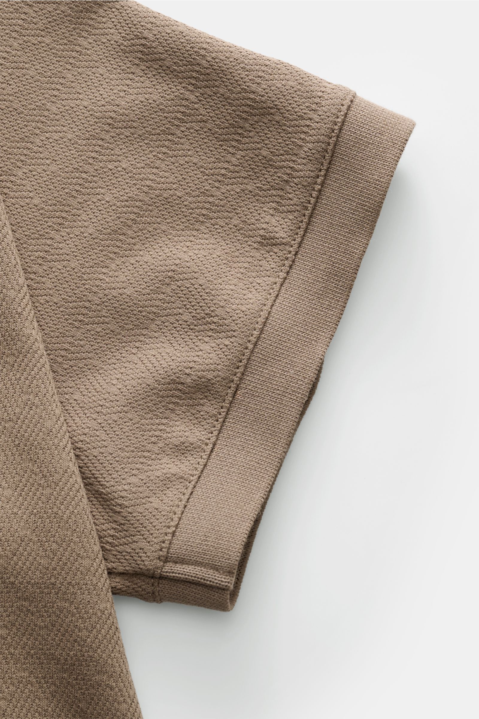 Nahaufnahme des taupefarbenen Emporio Armani Poloshirts aus Baumwoll-Jersey mit feiner Strukturoptik, Slim Fit, Polokragen, Drei-Knopf-Leiste und geradem Saum, fotografiert von der Ärmelperspektive.