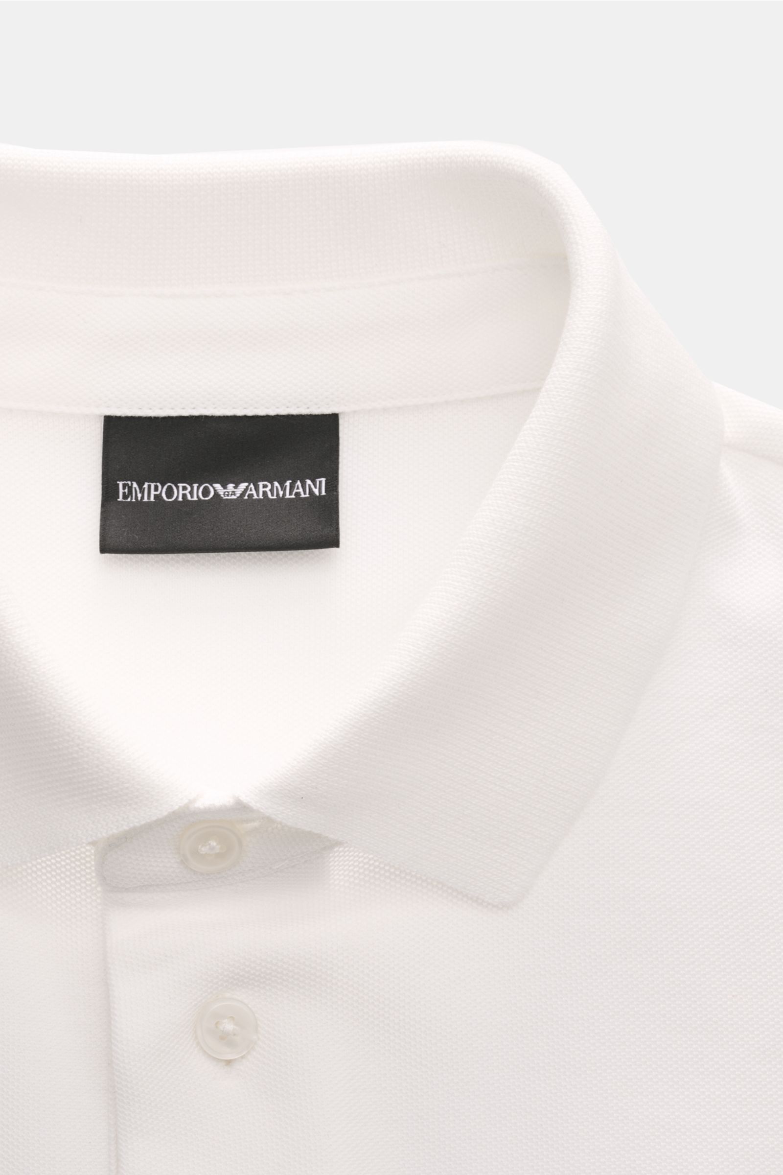 Close-up front view of Emporio Armani Poloshirt offwhite showing classic polo collar, buttons, and label stitching, made of pure cotton piqué jersey with regular fit and side slits. Vielseitiger Klassiker für sportive Looks: Das Poloshirt von EMPORIO ARMA