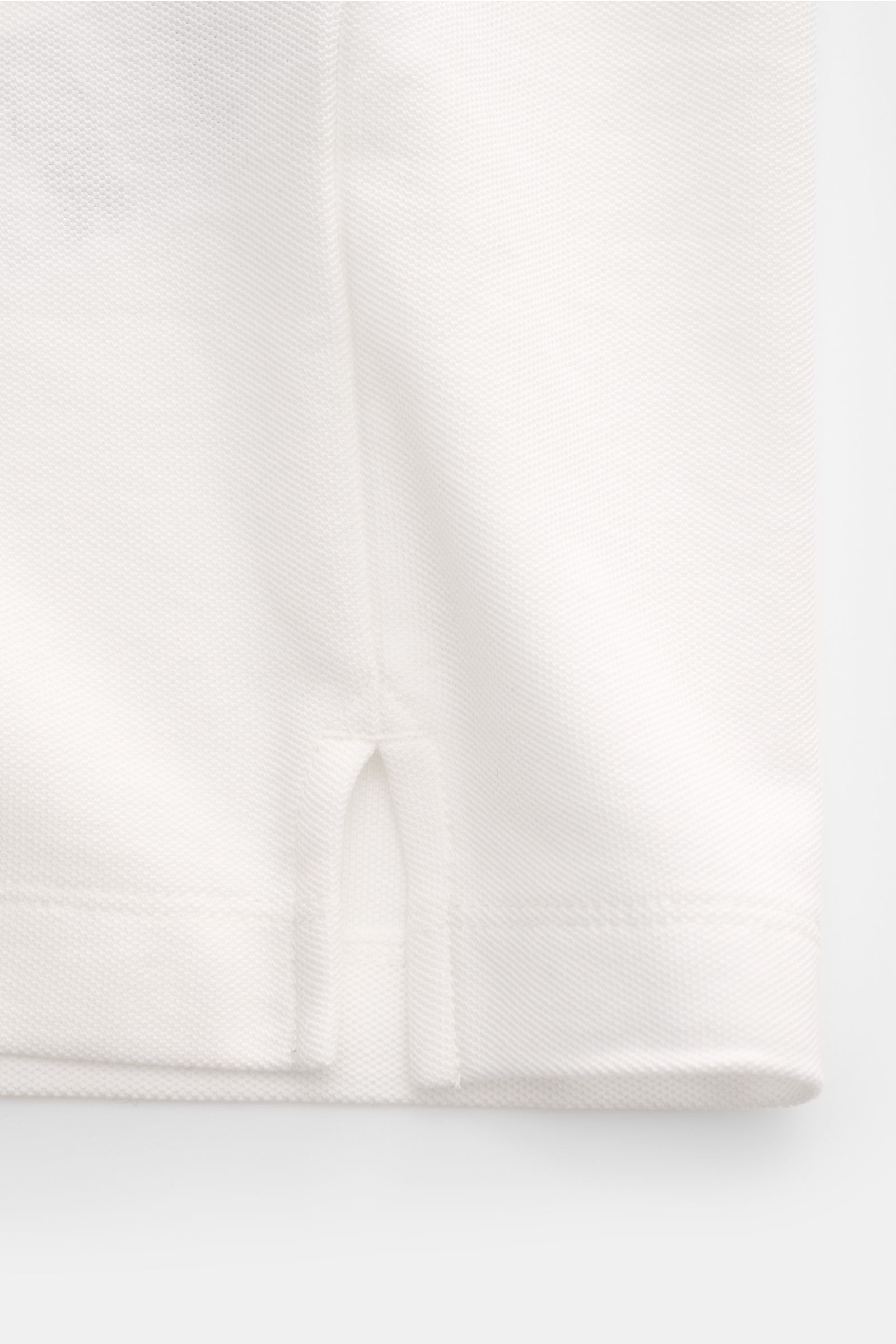 Close-up side hem view of the Emporio Armani Poloshirt offwhite, showcasing piqué cotton, regular fit, classic collar, label stitching, and side slits. Vielseitiger Klassiker für sportive Looks: Das Poloshirt von EMPORIO ARMANI überzeugt mit seinem zeitlo