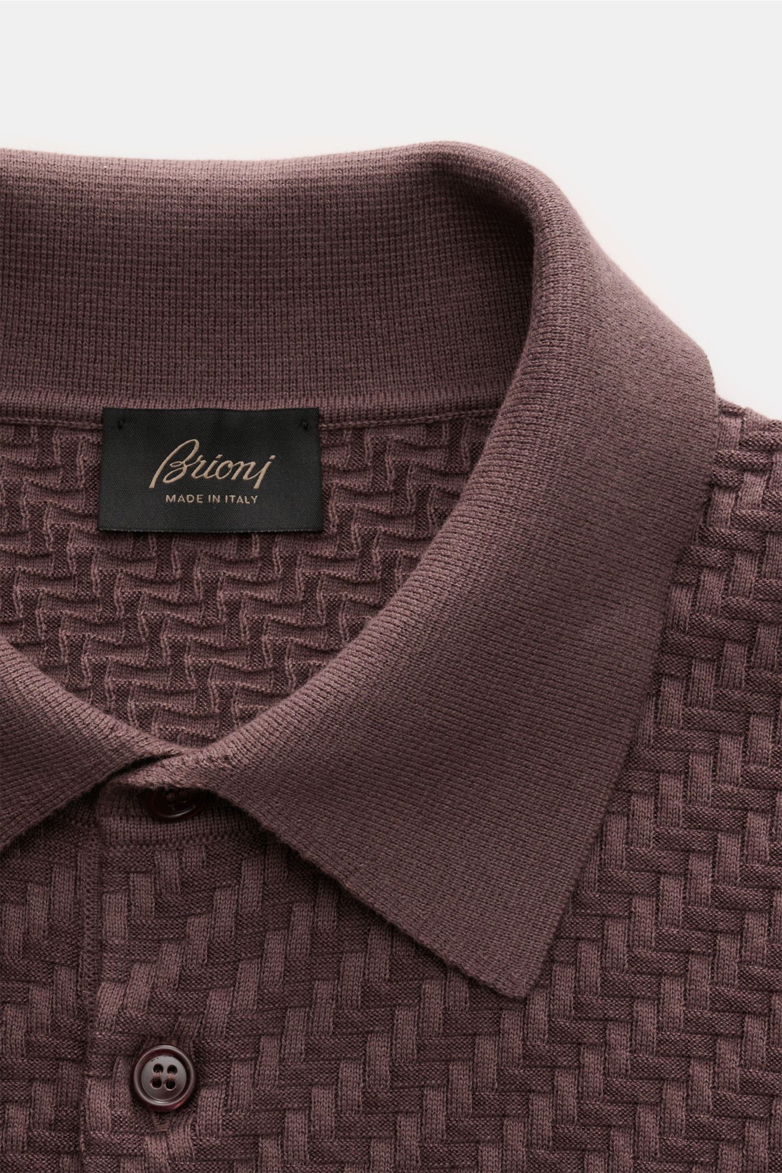 Nahaufnahme des Brioni Kurzarm-Strickpolo dunkelbraun von oben, mit Intreccio-Flechtmuster, Polokragen, Perlmutt-Knöpfen und Rippbündchen.