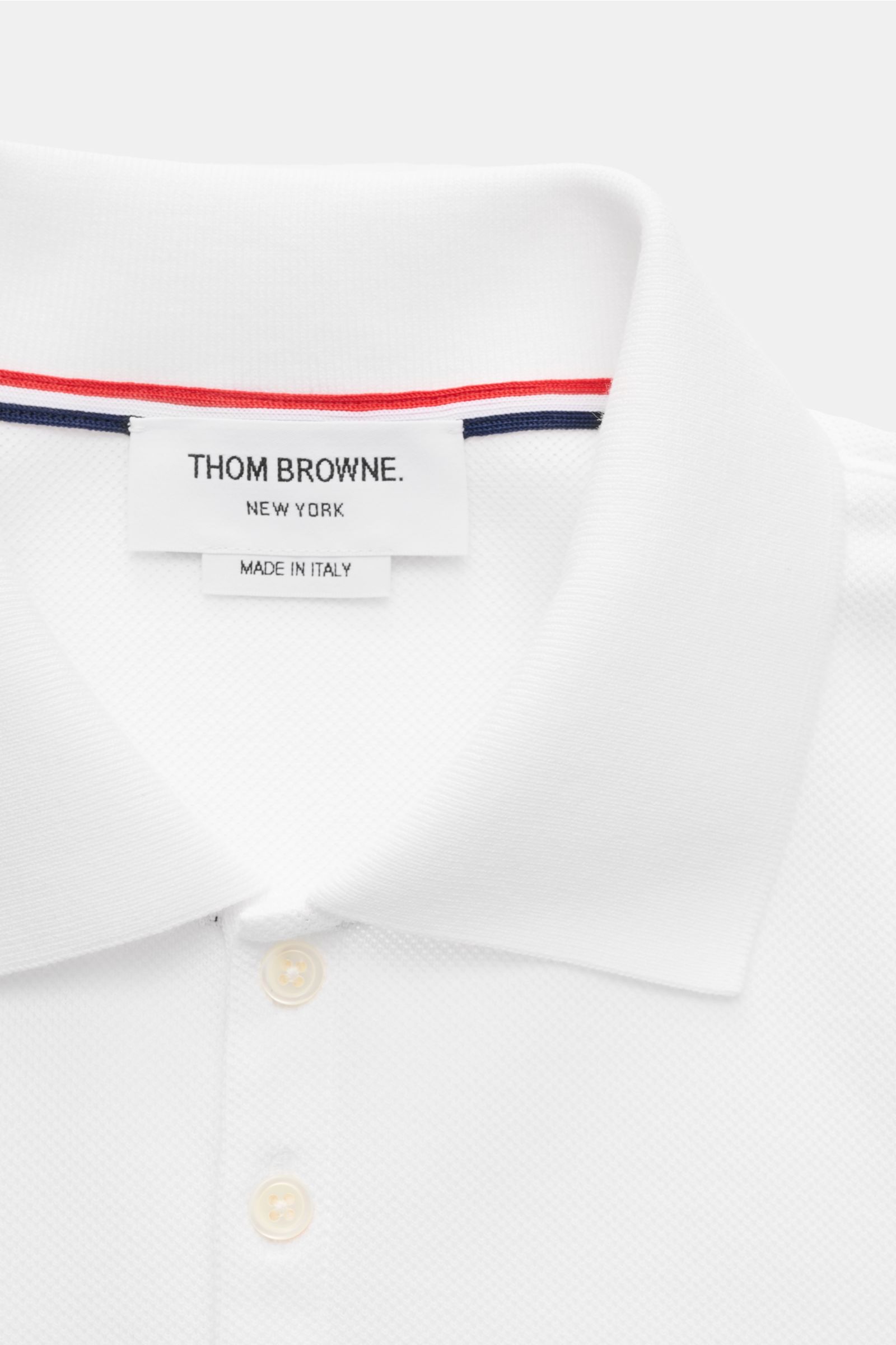 Close-up front view of the Thom Browne Polo shirt white showing the classic collar, five-button placket, and signature striped logo inside the collar. A modern essential: This polo shirt by THOM BROWNE is luxurious and comfortable, which makes it a sporty