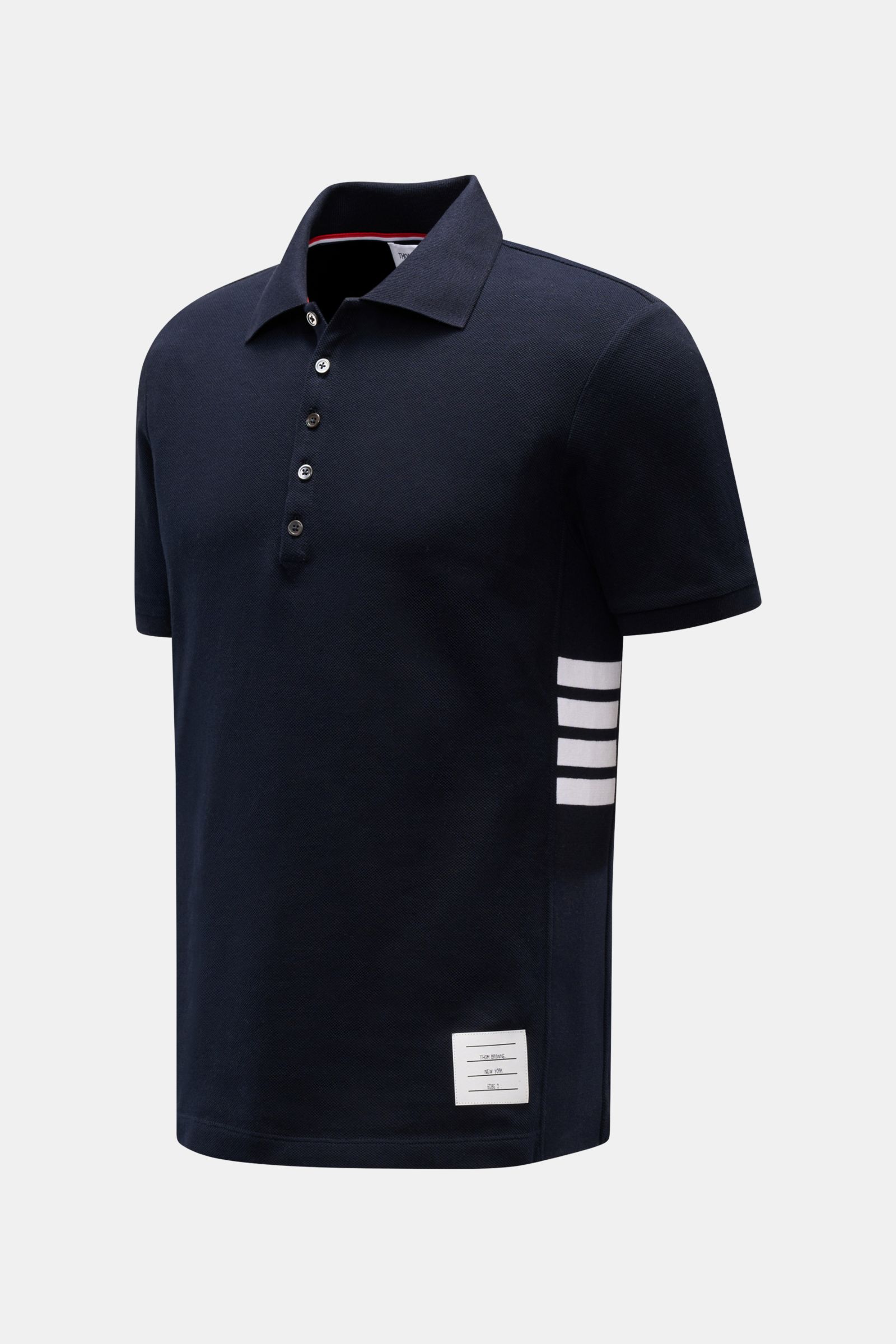 Thom Browne Poloshirt navy in Slim Fit aus reiner Baumwolle, seitlich mit Streifenlogo, Fünf-Knopf-Leiste, Rippbündchen, schräg von vorne.