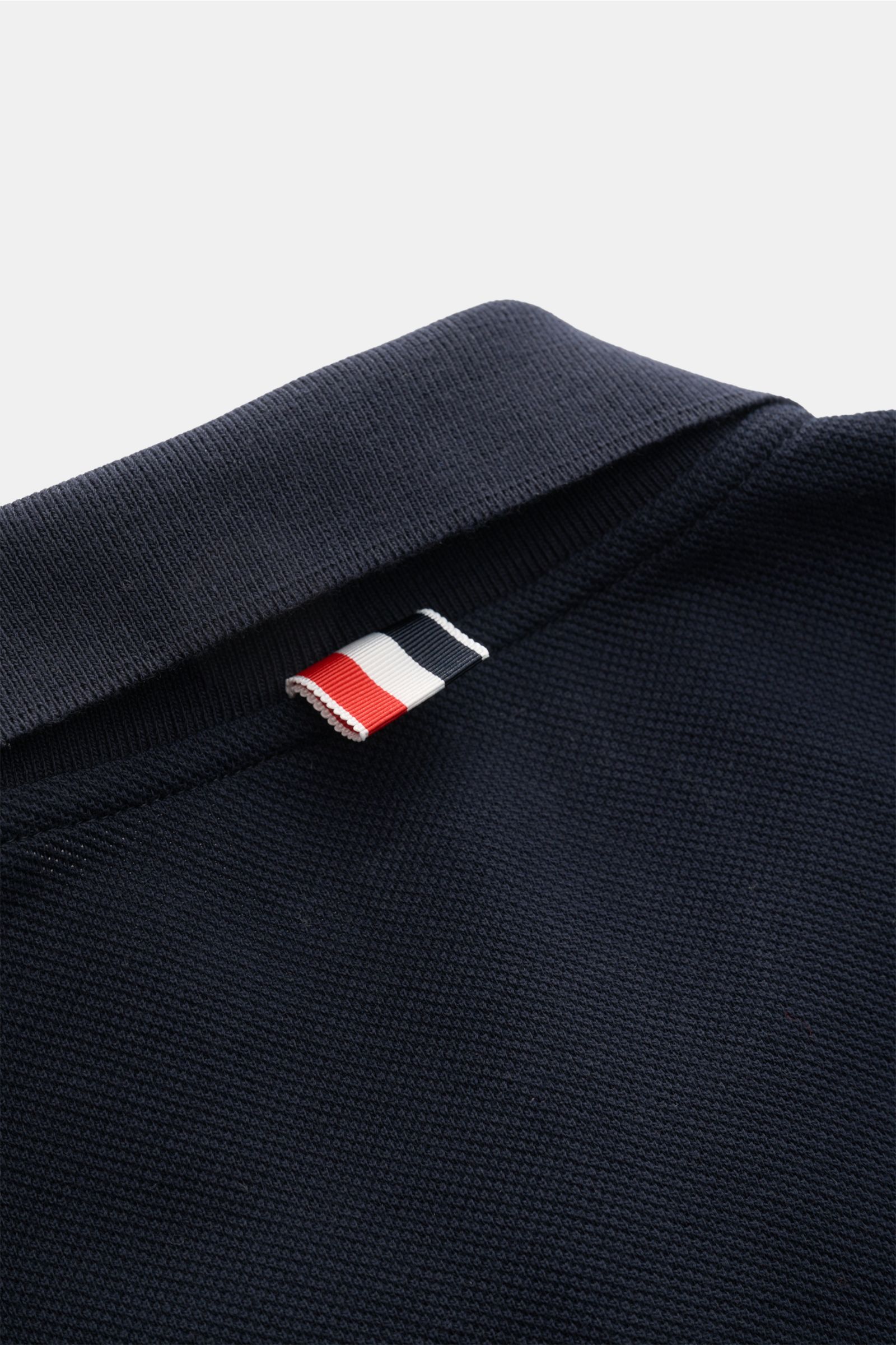 Nahaufnahme des Kragens vom Thom Browne Poloshirt navy aus reiner Baumwolle mit markentypischem Streifen-Logo, Slim Fit, Rippbündchen und elastischen Seiteneinsätzen.