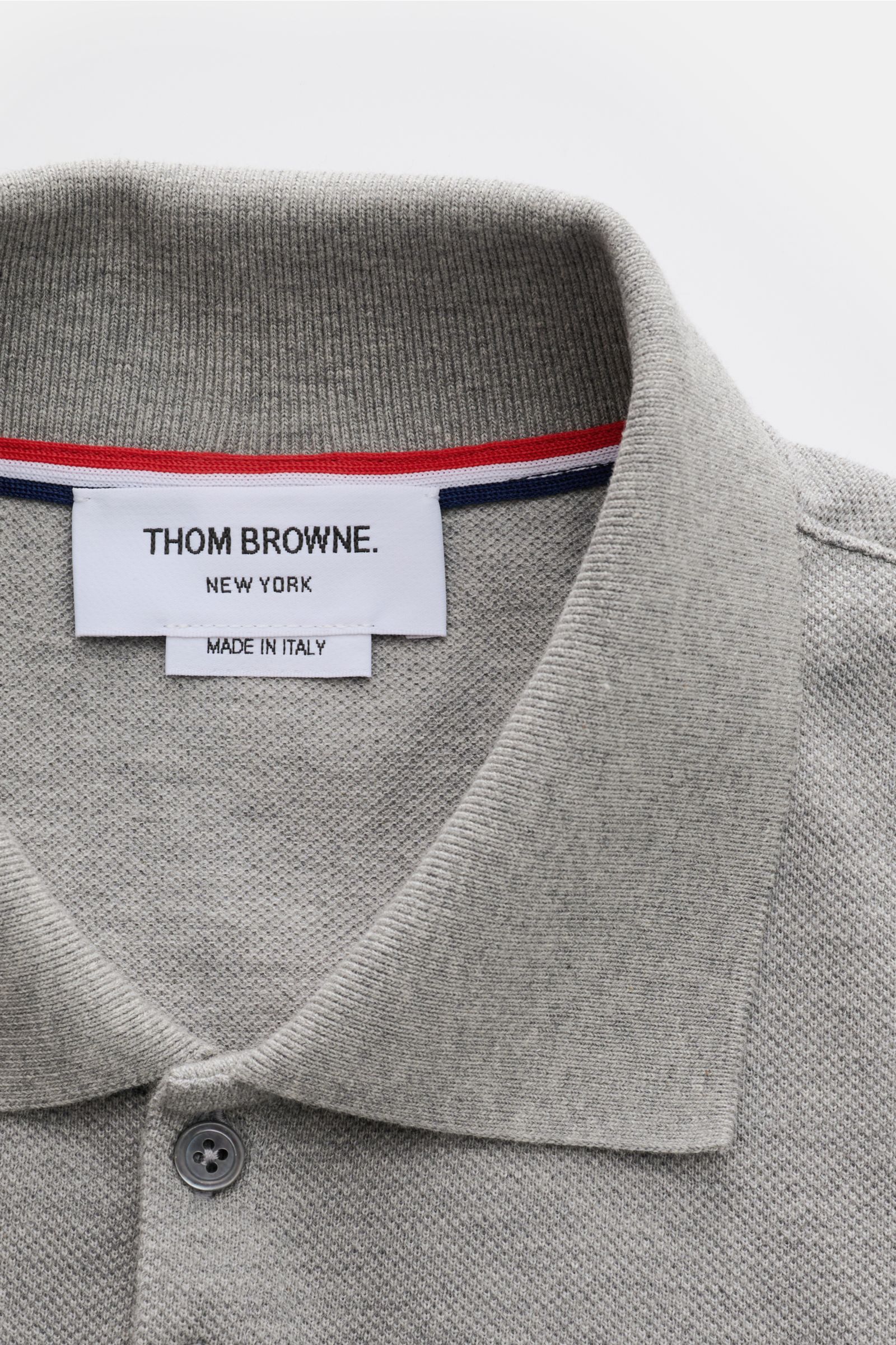 Close-up front view of Thom Browne Polo shirt grey mottled collar and label, featuring pure cotton, slim fit, five-button placket, ribbed cuffs, stretchy side inserts, and signature striped logo. A modern essential: This polo shirt by THOM BROWNE is luxur