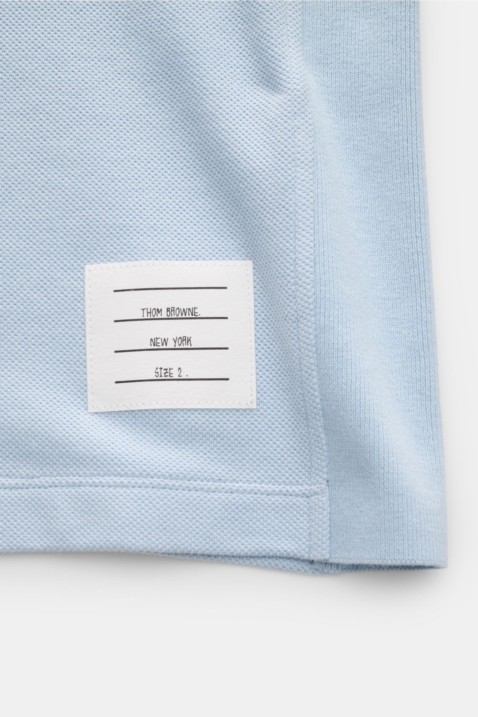 Alt-Tag (124 Zeichen):
Detailansicht des Thom Browne Poloshirts hellblau aus reiner Baumwolle mit markentypischem Streifen-Logo und strukturierter Oberfläche.
