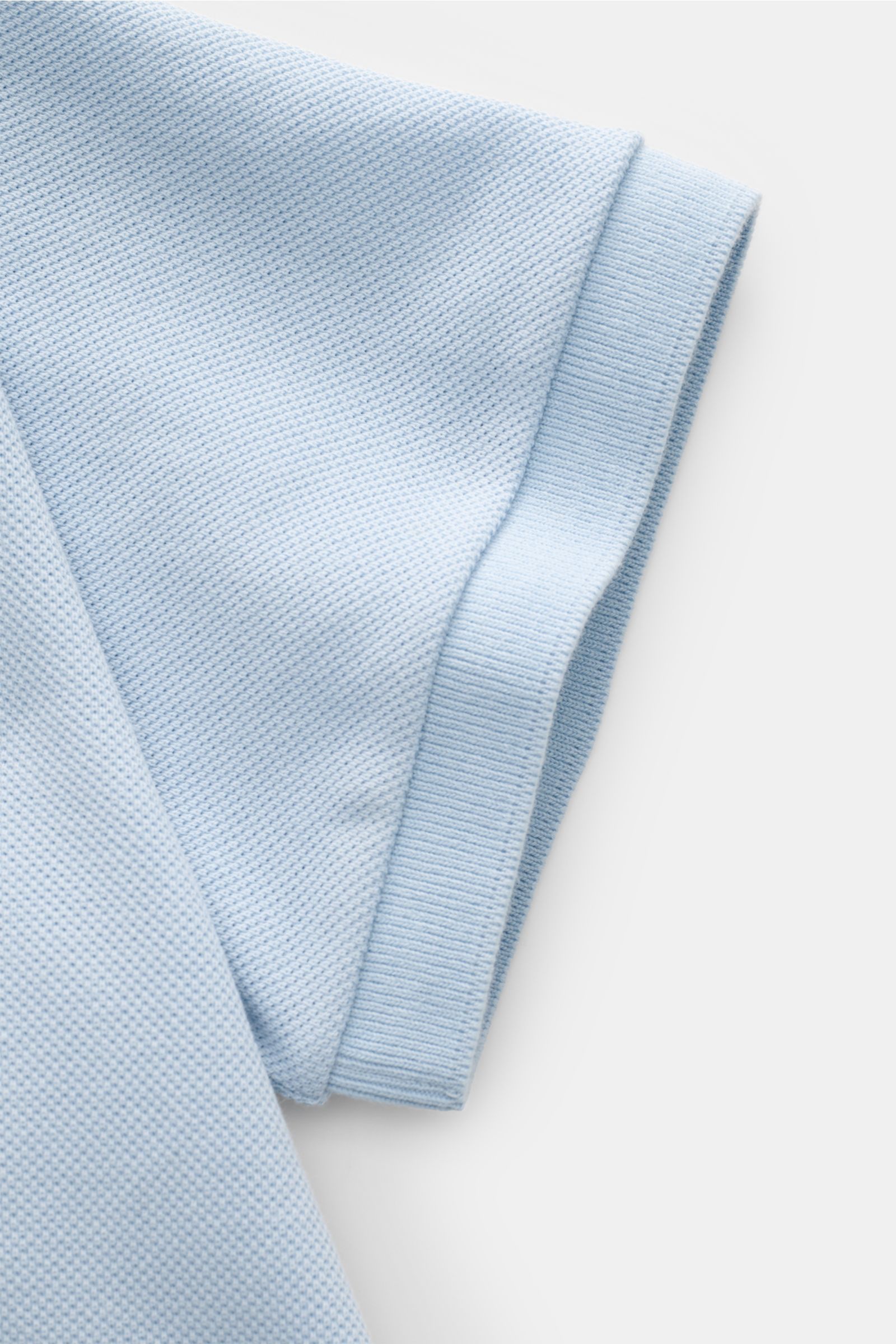 Nahaufnahme des Thom Browne Poloshirts hellblau, zeigt Ärmel mit Rippbündchen und fein strukturierte reine Baumwolle.