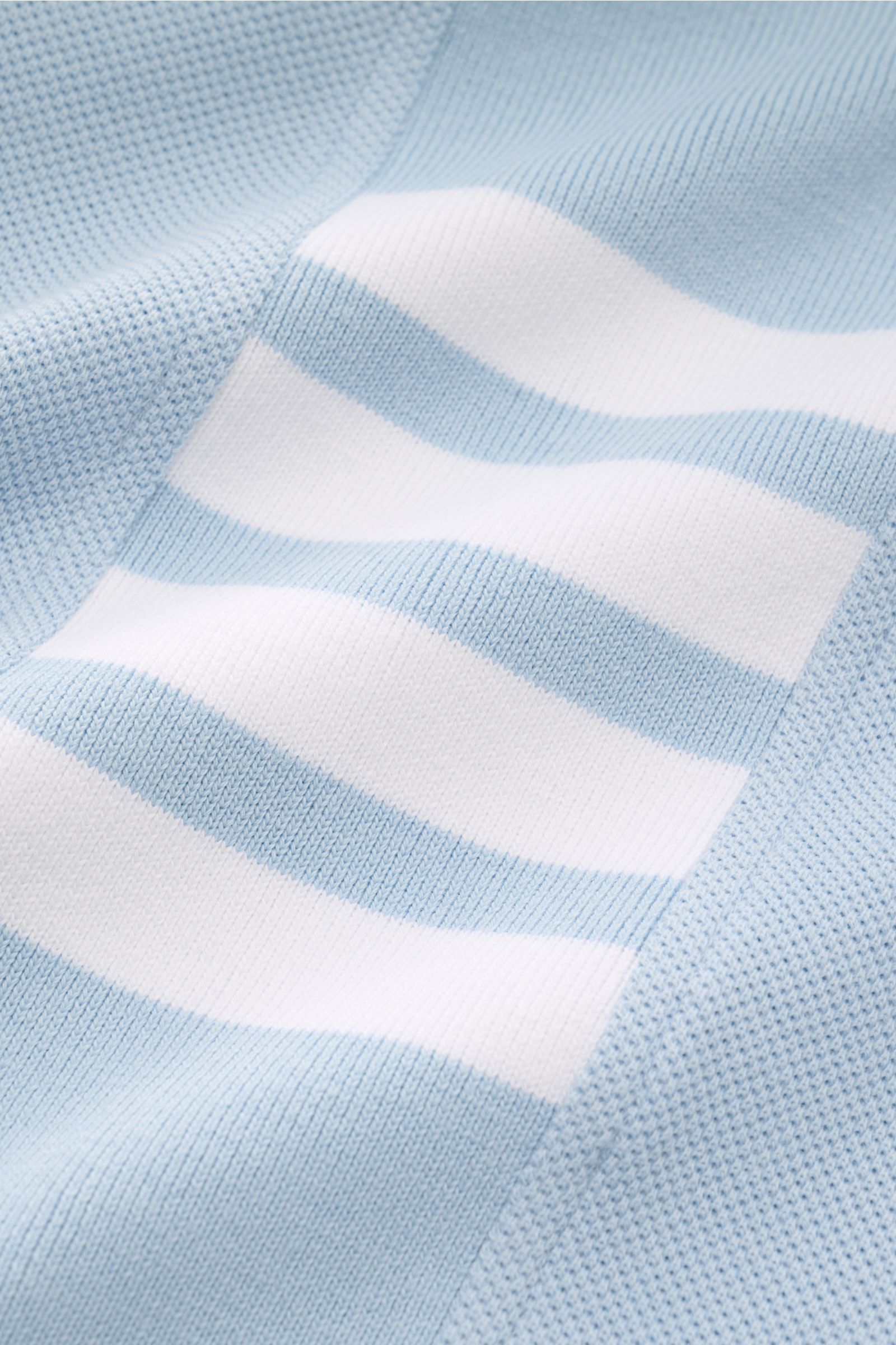 Nahaufnahme des Thom Browne Poloshirts hellblau mit markentypischem weißen Streifenlogo und leicht griffiger Baumwollstruktur.
