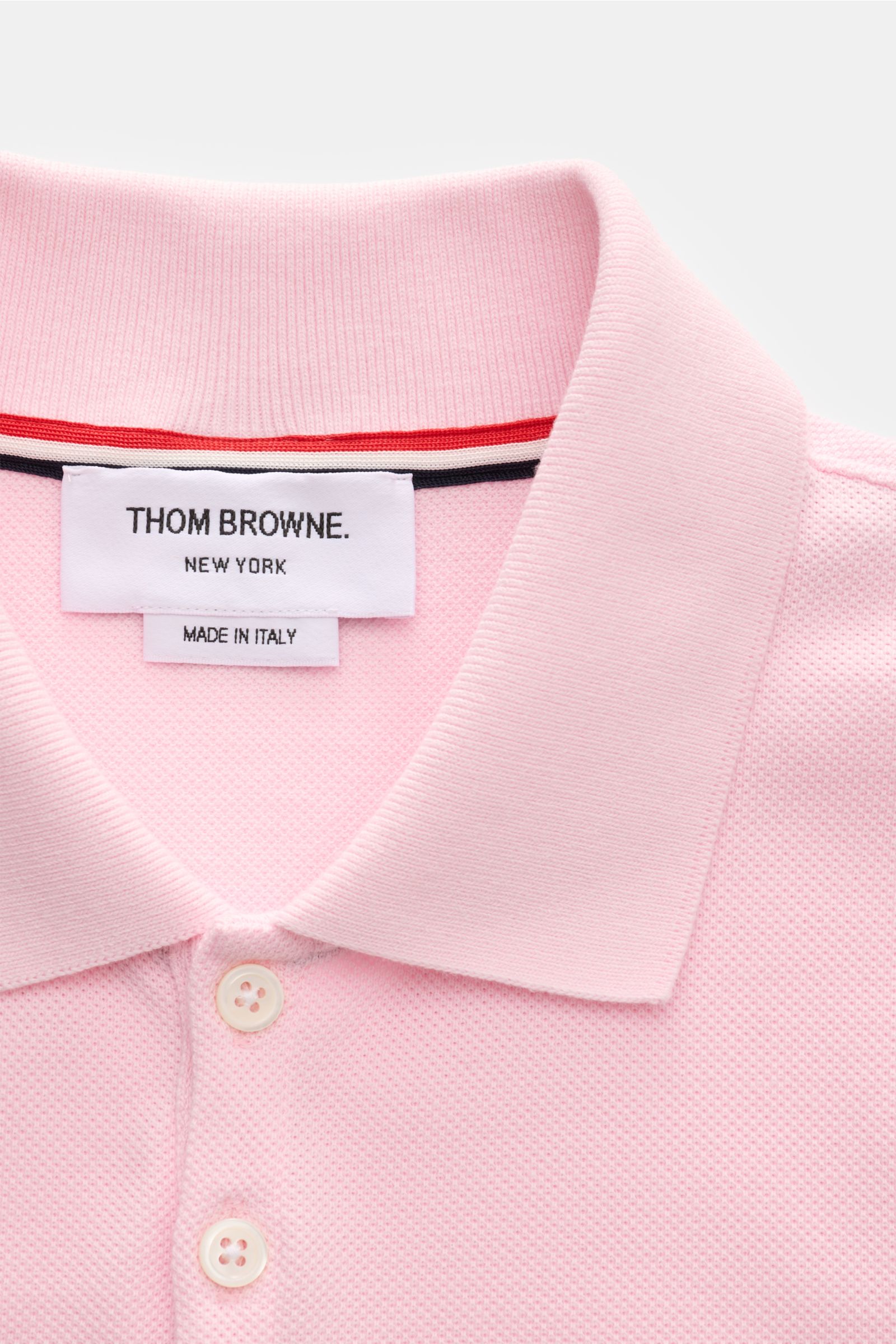 Close-up front view of Thom Browne Poloshirt rosé, showcasing slim fit, pure cotton, classic collar, five-button placket, ribbed cuffs, elastic side inserts, and signature stripe logo.