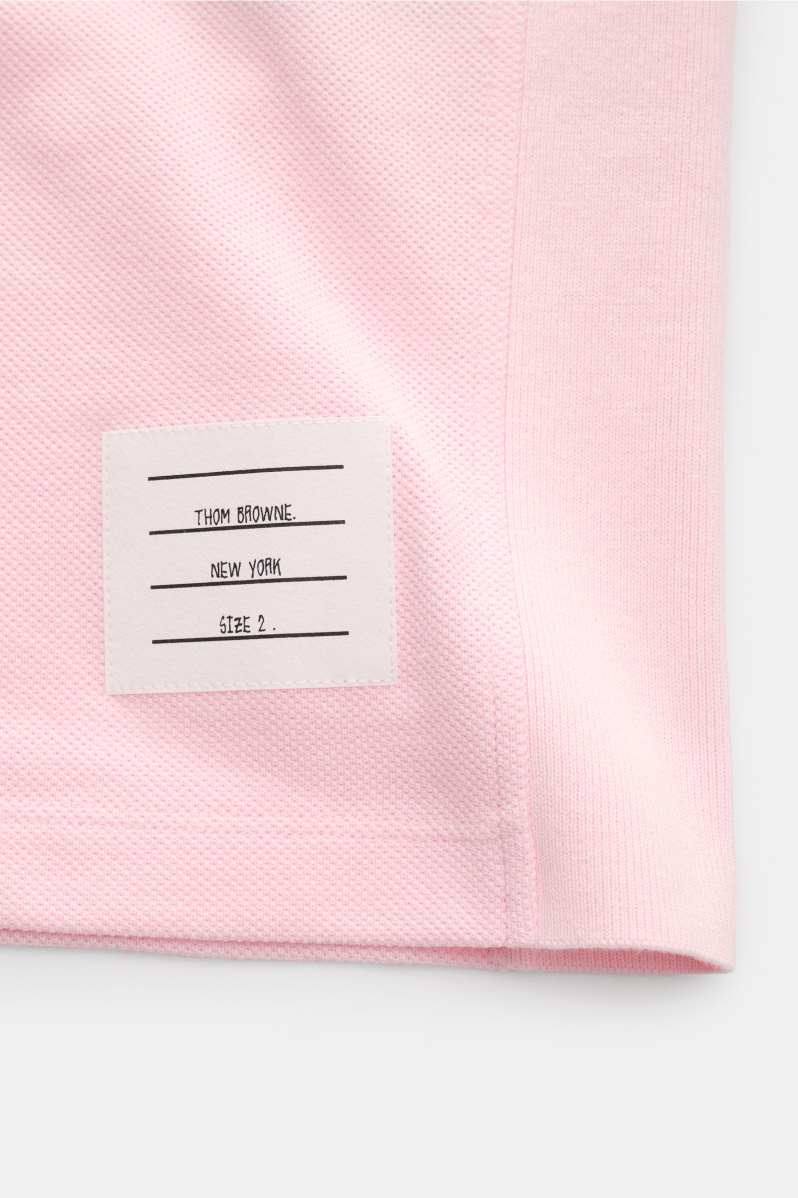 Close-up from the side of the lower hem of the Thom Browne Poloshirt rosé in pure cotton with a textured fabric and stitched label.

Description including provided content:
Modernes Essential: Das Poloshirt von THOM BROWNE besticht mit luxuriösem Trage