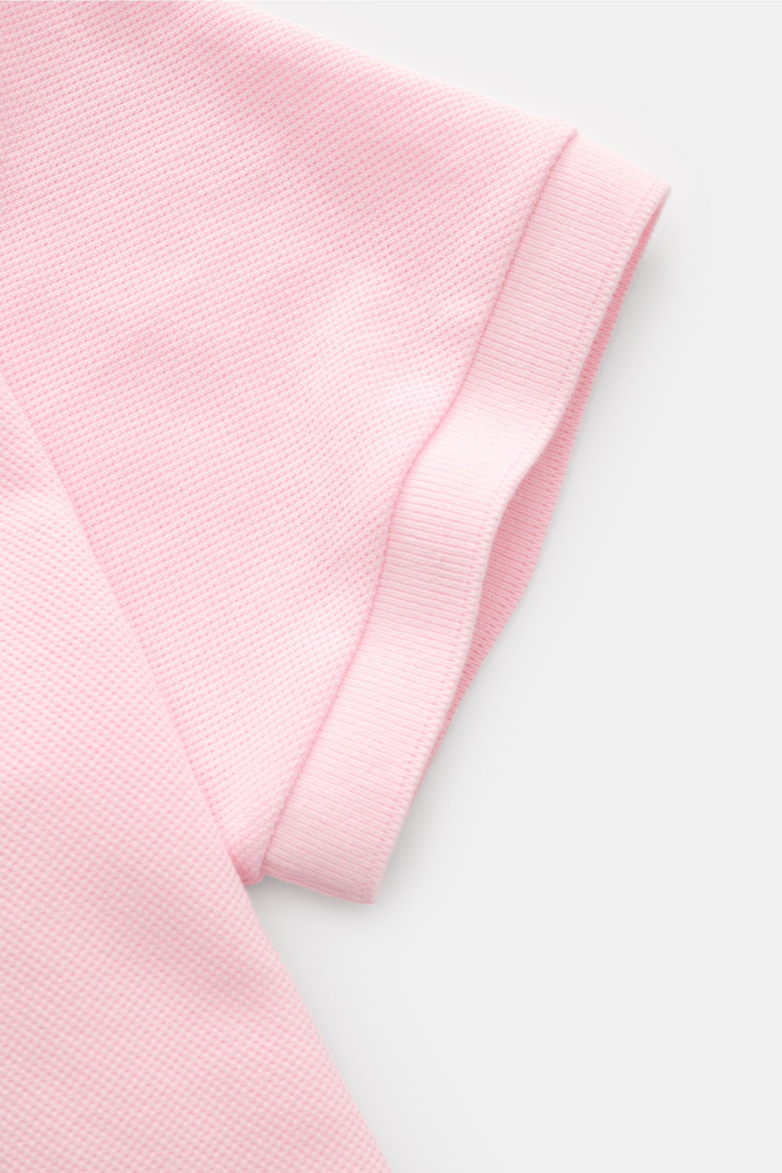 Close-up side view of the sleeve of the Thom Browne Poloshirt rosé in pure cotton with a slim fit, ribbed cuffs, and textured fabric. Modernes Essential: Das Poloshirt von THOM BROWNE besticht mit luxuriösem Tragekomfort und wird so zum sportiv-eleganten 