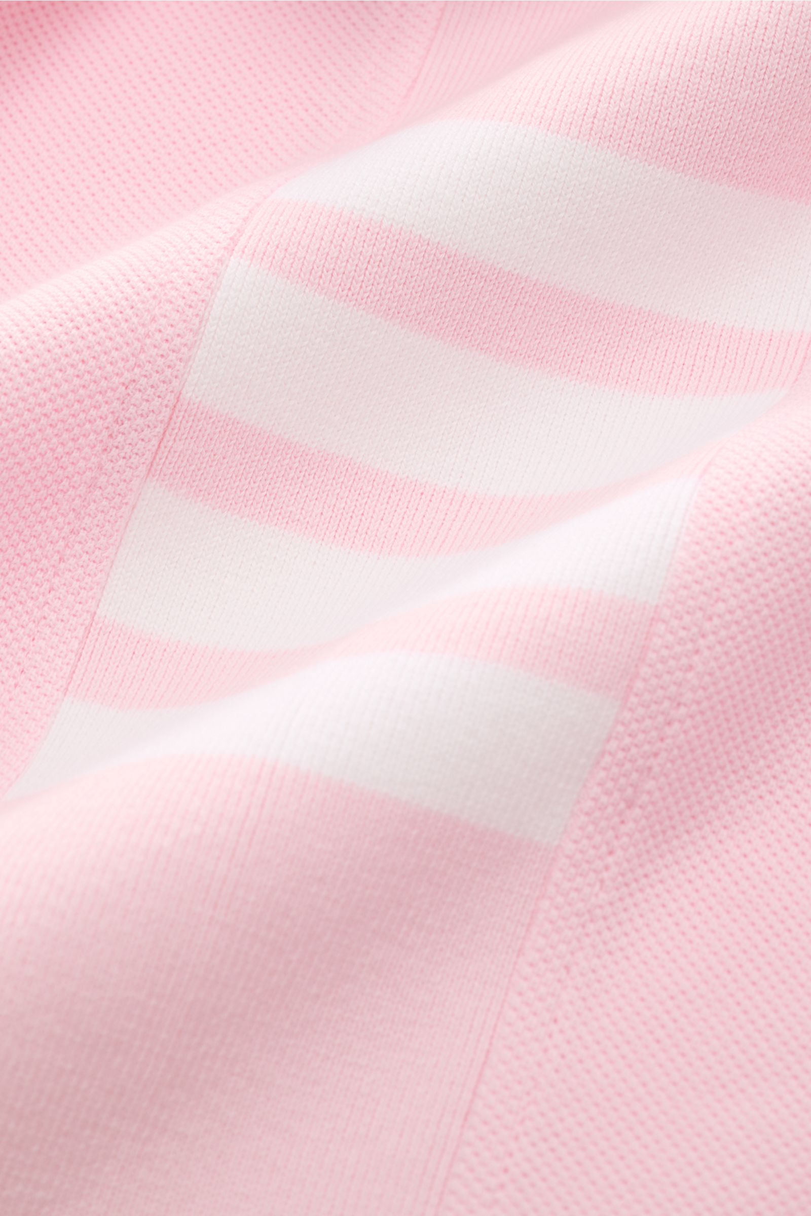 Close-up of Thom Browne Poloshirt rosé showing pink and white striped pattern and textured cotton fabric from a detailed side perspective, highlighting its premium knit and soft structure. Modernes Essential: Das Poloshirt von THOM BROWNE besticht mit lux