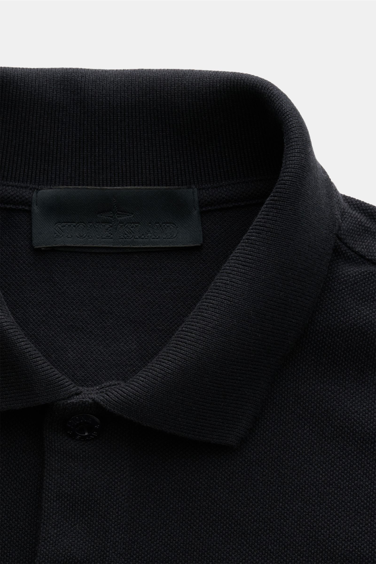 Nahaufnahme aus schräger Perspektive des Stone Island Poloshirt 'Ghost Piece' navy mit typischem Polokragen, Zwei-Knopf-Leiste, tonalem Weblabel aus reinem Baumwoll-Piqué.