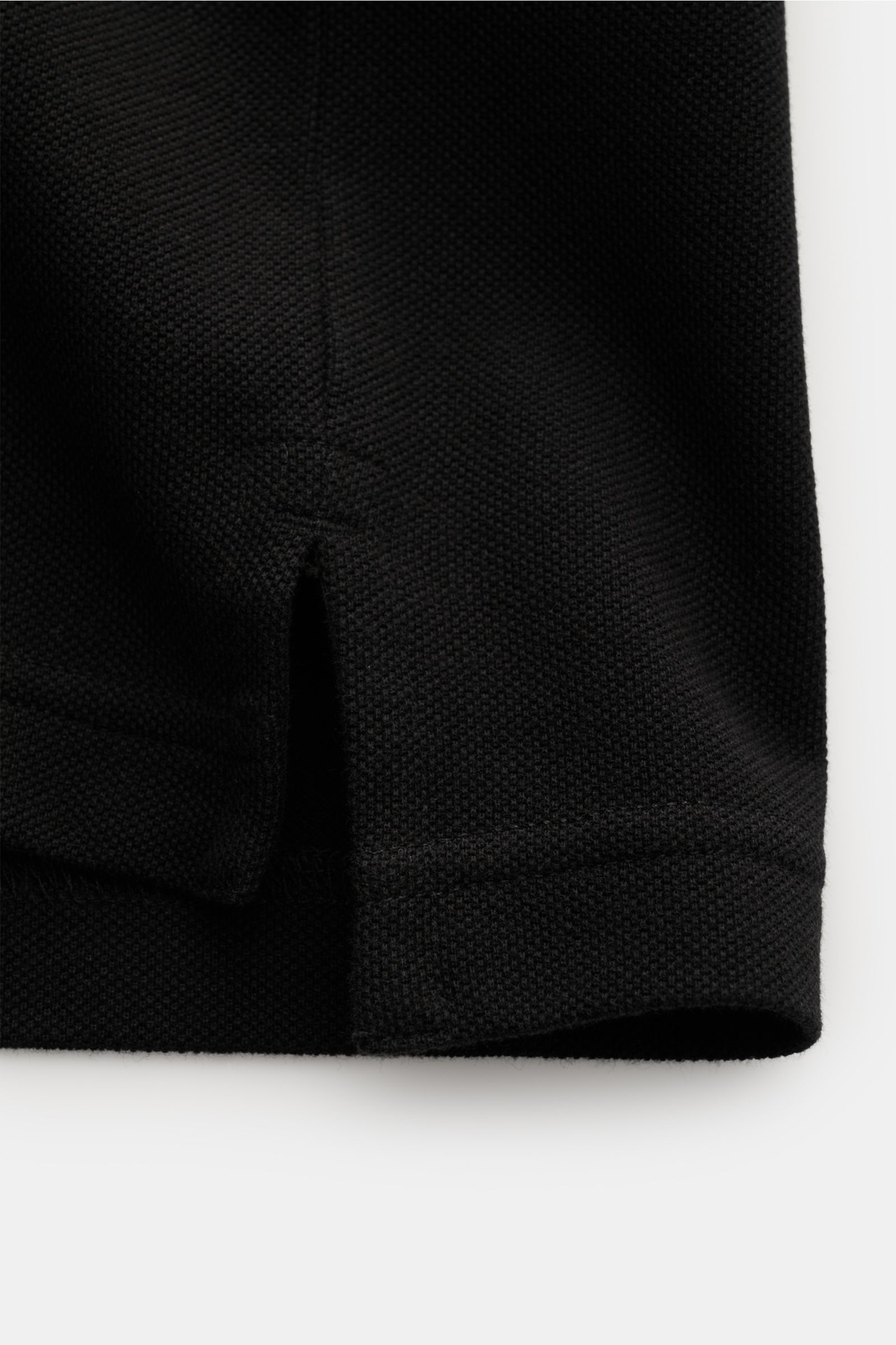 Nahaufnahme des unteren Saumteils des Stone Island Poloshirts 'Ghost Piece' schwarz, Slim Fit aus reiner Baumwoll-Piqué mit seitlichem Saumschlitz, fotografiert von vorne unten.