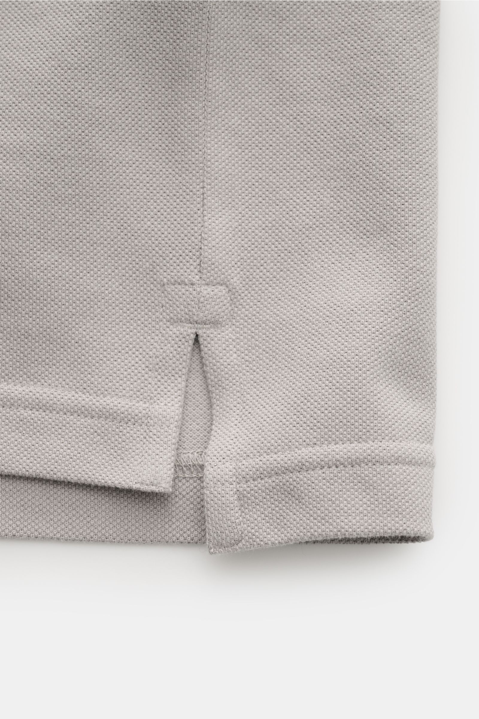 Nahaufnahme des unteren Saumbereichs des Stone Island Poloshirts 'Ghost Piece' grau, slim fit mit seitlichem Saumschlitz und leicht körnigem Baumwoll-Piqué.