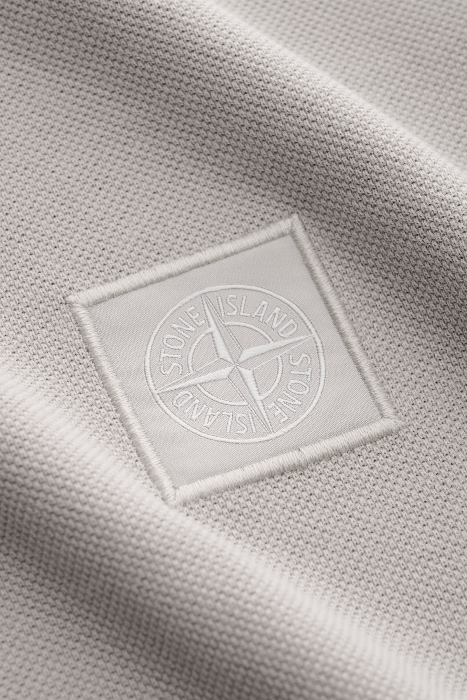 Nahaufnahme des tonalen STONE ISLAND-Weblabels auf dem Stone Island Poloshirt 'Ghost Piece' grau aus Baumwoll-Piqué mit leicht körnigem Griff.