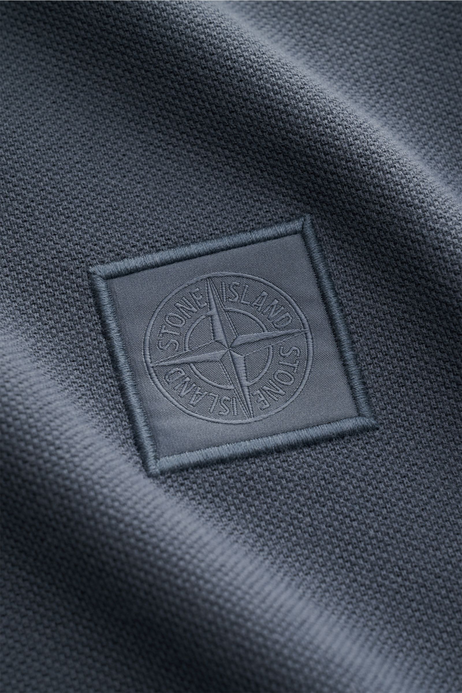 Nahaufnahme des tonalen STONE ISLAND-Weblabels auf dem Stone Island Poloshirt 'Ghost Piece' graublau aus reiner Baumwolle Piqué.