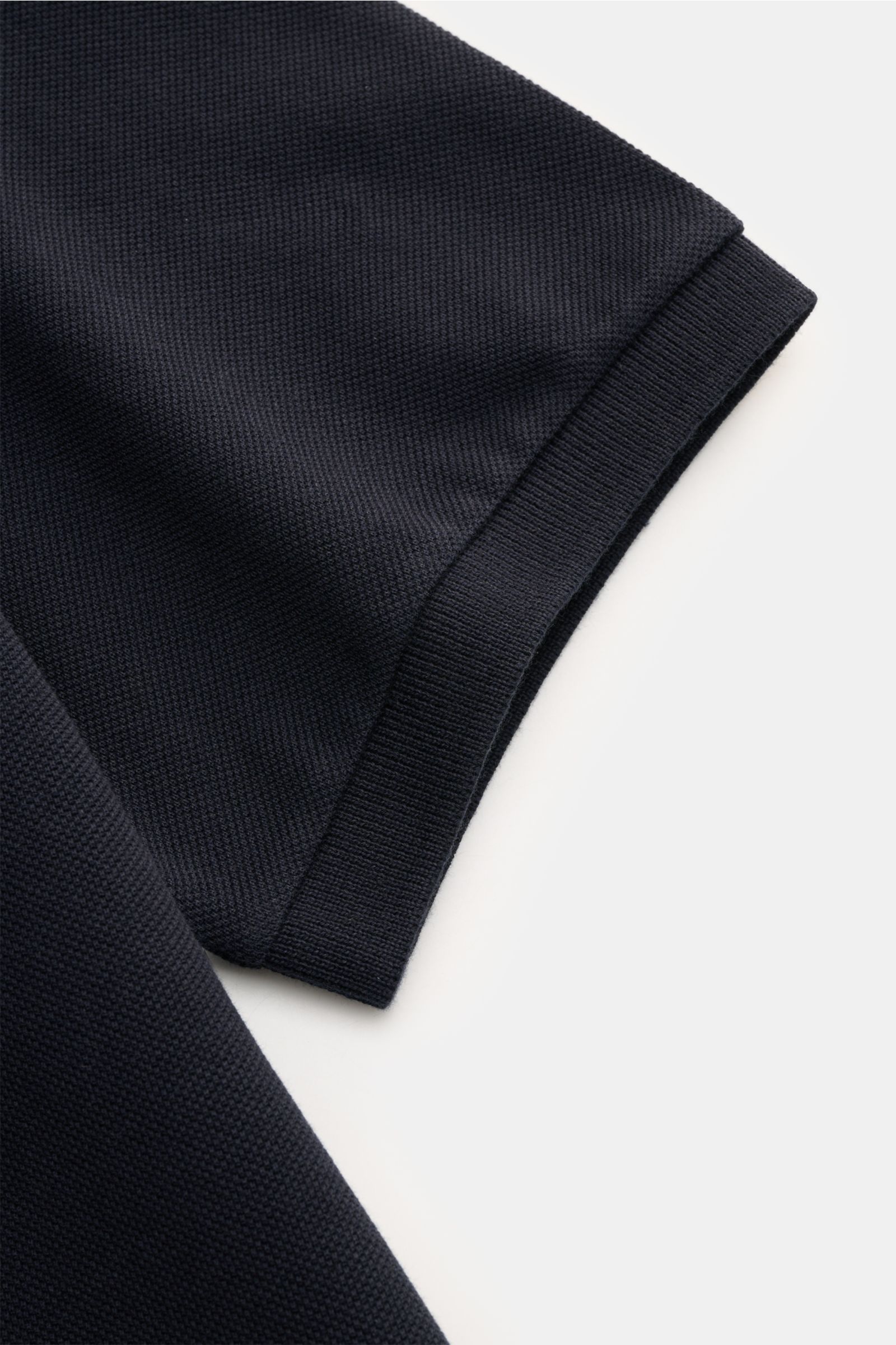 Close-up of Stone Island Poloshirt navy sleeve with textured pure cotton piqué fabric, flexible cuff, and side hem slit, photographed from above.
