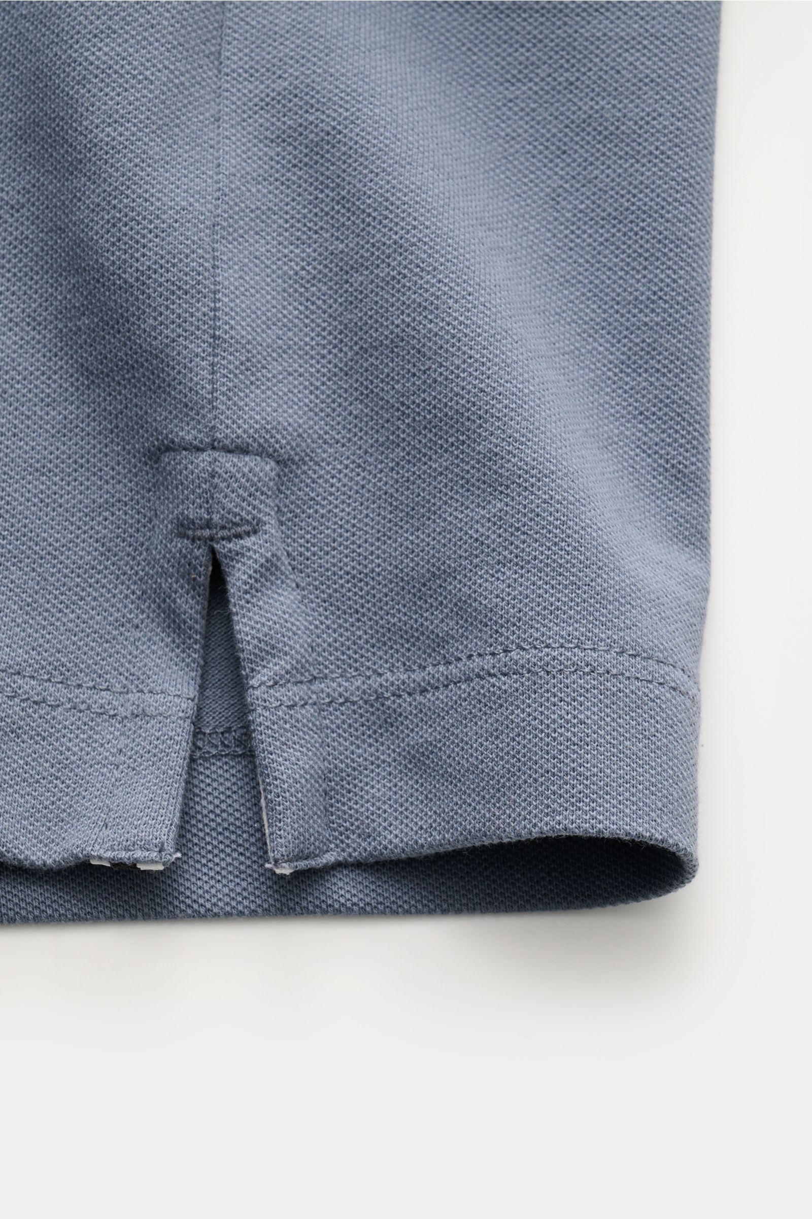 Close-up side view of the hem and side slit of the Stone Island Poloshirt graublau, made of elastic cotton piqué fabric with a soft touch. Das moderne Piqué-Poloshirt von STONE ISLAND mit schmalen Kontraststreifen ist ein vielseitiger Klassiker aus ela