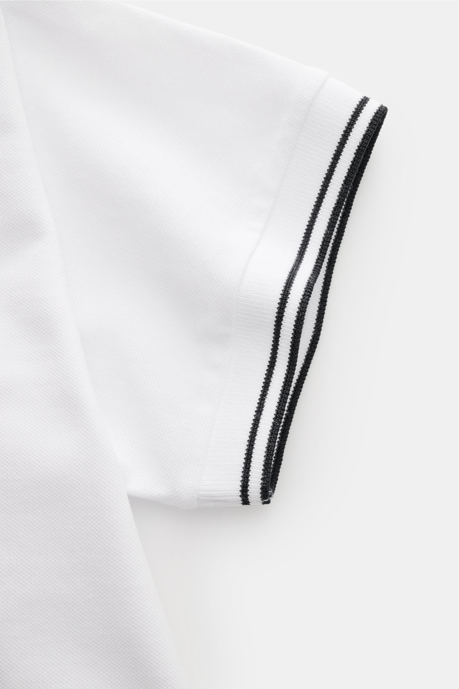 Stone Island Poloshirt weiß in Nahaufnahme, Detail des elastischen, weißen Piqué-Stoffs mit schwarzen schmalen Kontraststreifen am Ärmelrand.