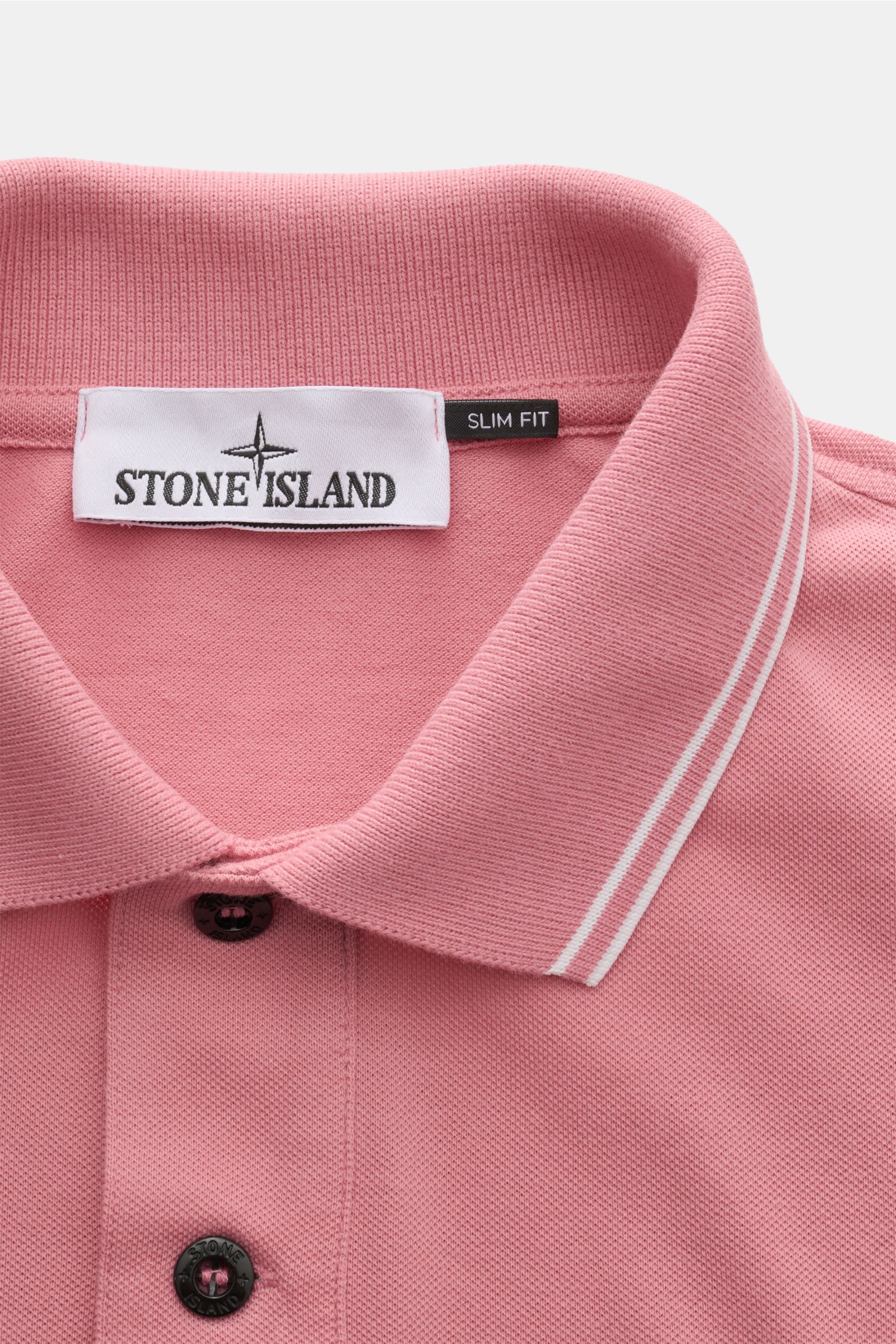 Nahaufnahme des Stone Island Poloshirts rosé aus elastischer Baumwolle in Slim Fit, mit schmalen weißen Kontraststreifen am Polokragen, aufgesetzter Knopfleiste und STONE ISLAND-Weblabel, fotografiert von oben.