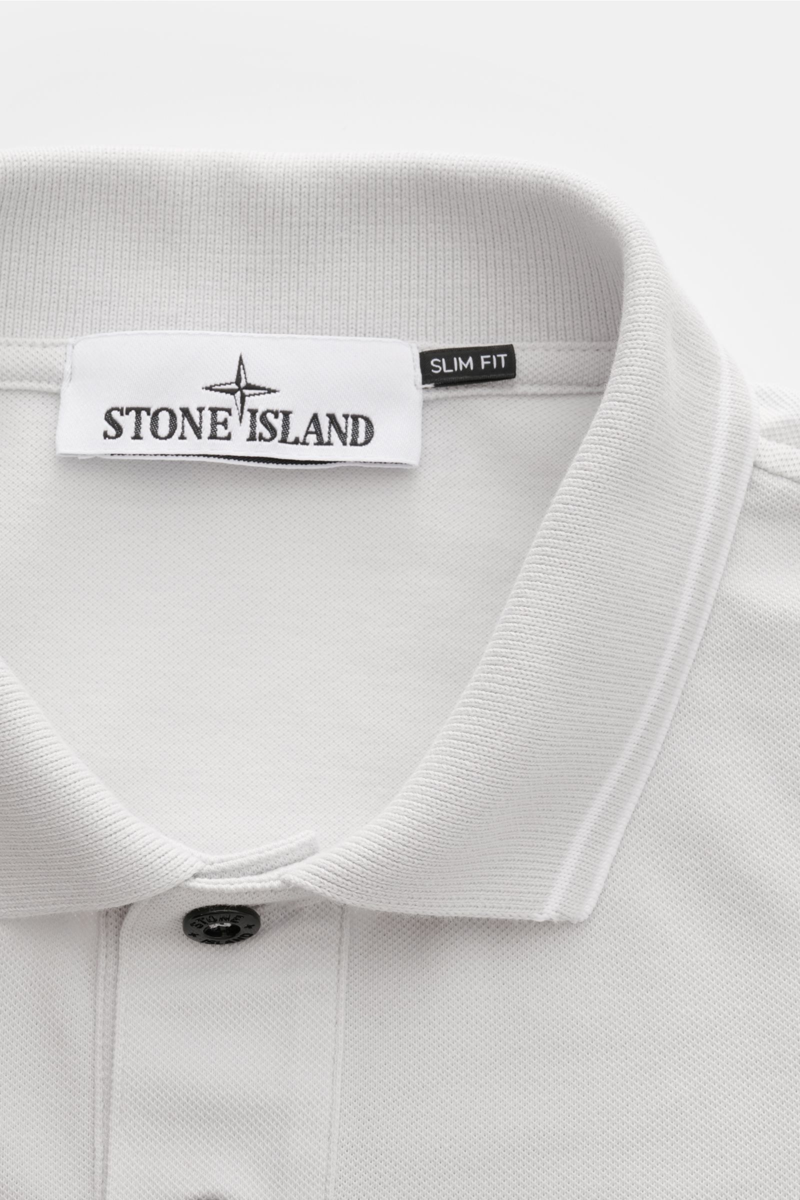 Nahaufnahme des Kragens und der Knopfleiste des Stone Island Poloshirt sand aus elastischer Baumwolle mit slim Fit und schmalen Kontraststreifen, fotografiert von oben.