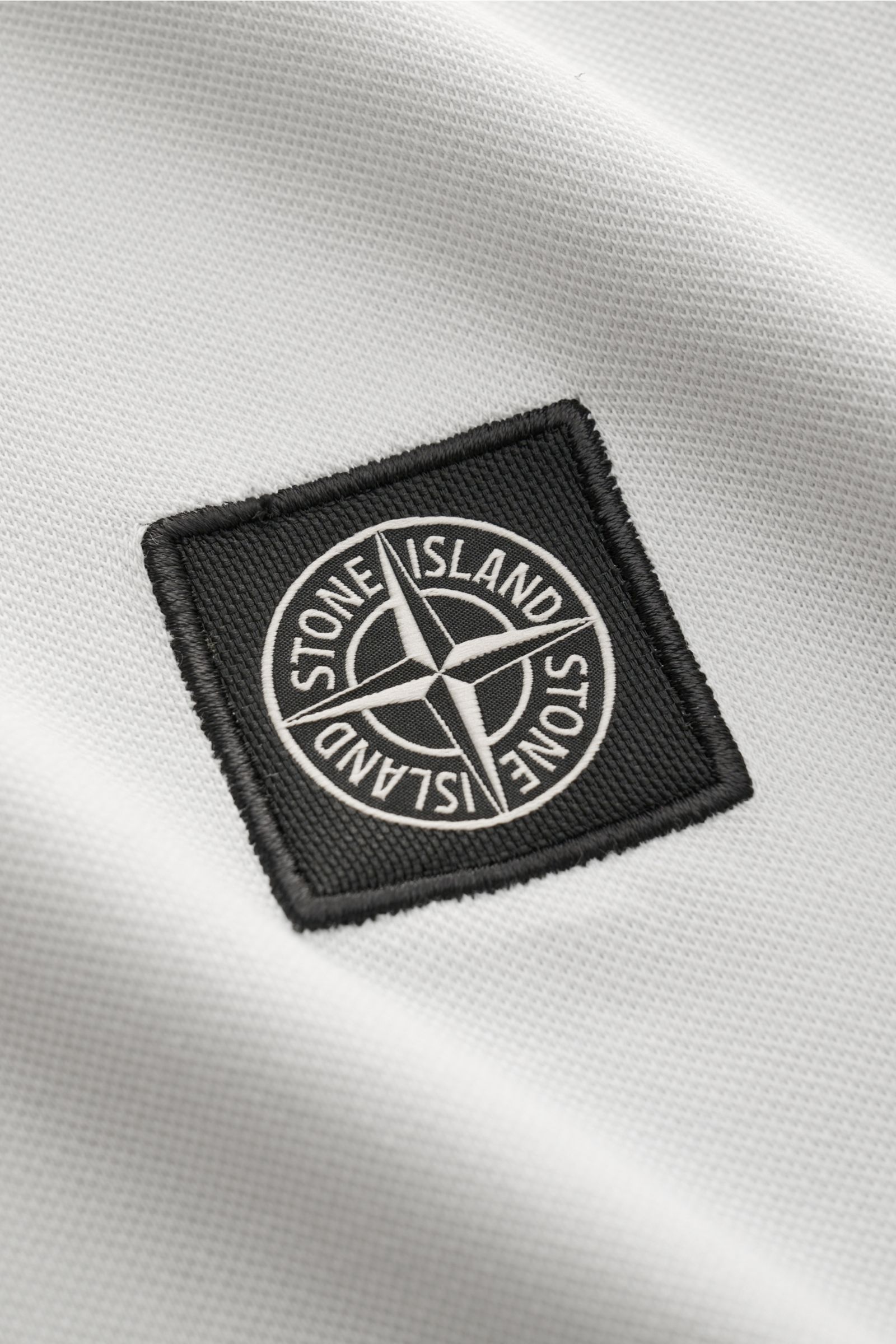 Stone Island Poloshirt sand, Detailaufnahme des schwarzen Weblabels auf weißem, elastischem Piqué aus Baumwolle mit weichem Griff.