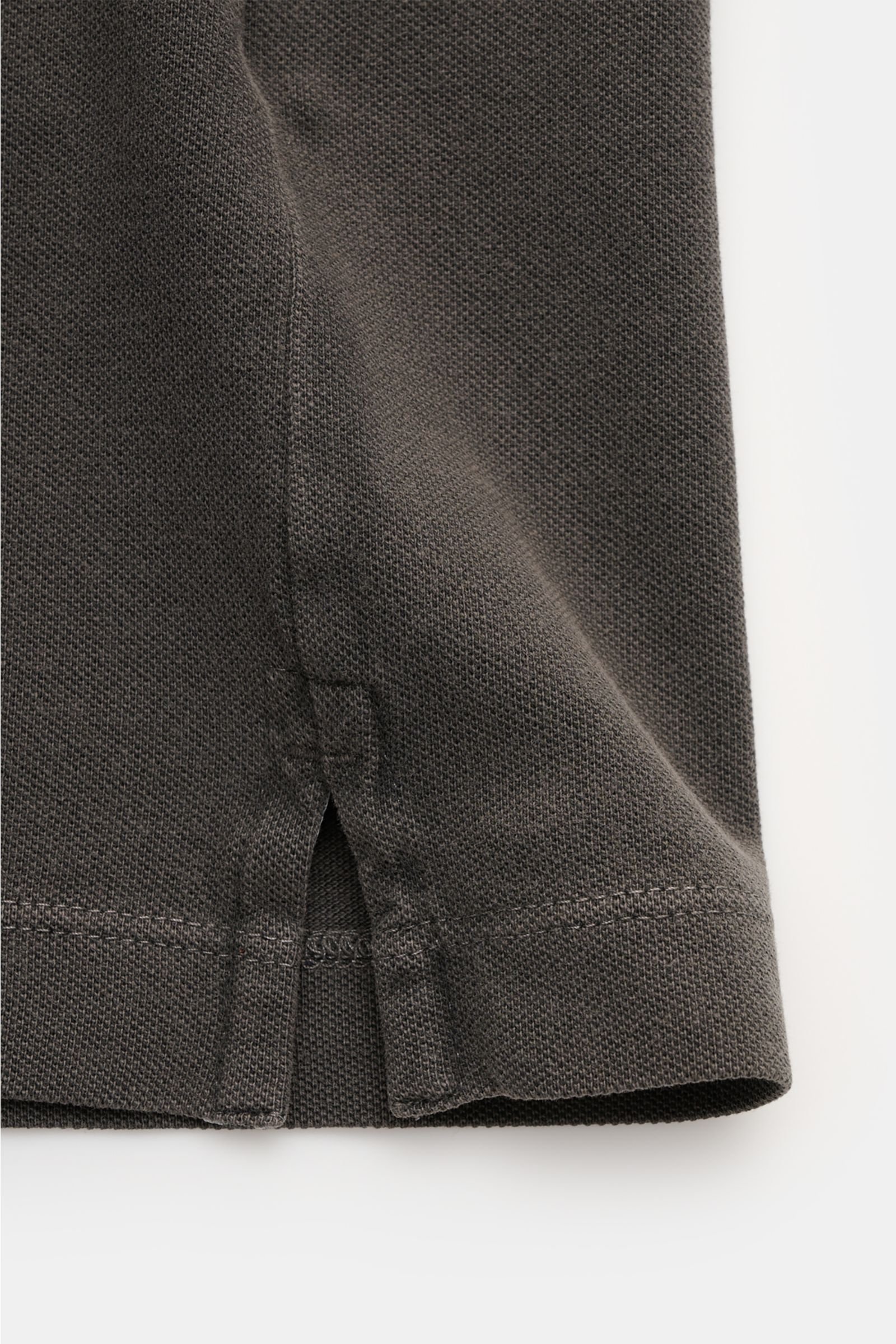 Nahaufnahme des Stone Island Poloshirts dunkelgrau von unten, Detail der kurzen Saumschlitze aus elastischer Baumwolle mit weichem Griff.