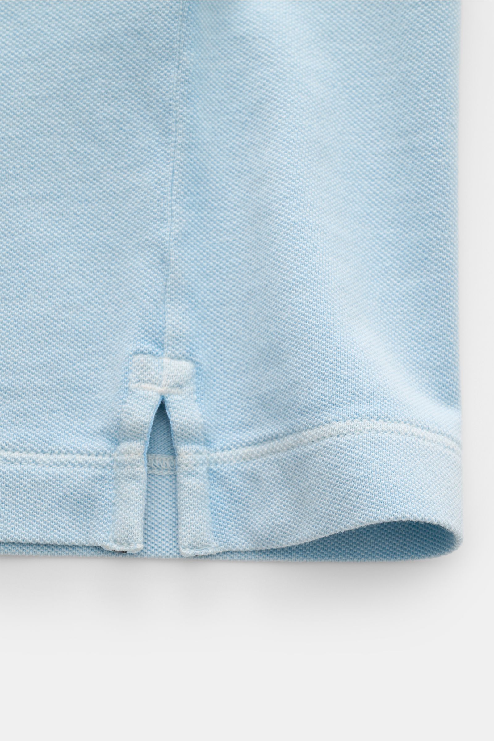 Nahaufnahme des Stone Island Poloshirts hellblau, blick auf seitlichen Saumschlitz und Piqué-Baumwollstruktur, Slim Fit, garment dyed.