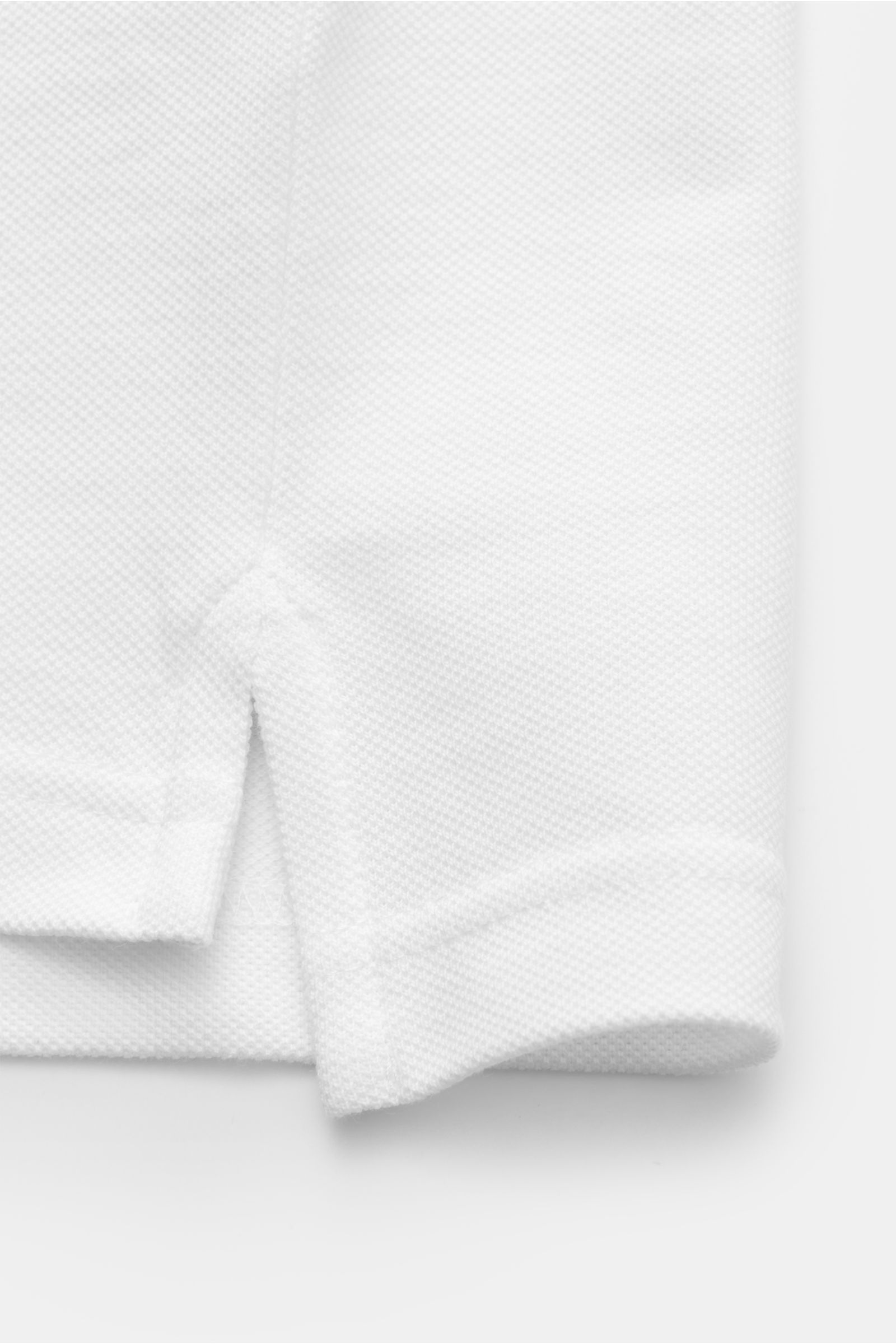 Close-up side view of the hem of the Belstaff Poloshirt weiß, showing piqué pure cotton fabric with a lightly textured feel, slim fit, two-button placket, classic polo collar, BELSTAFF web label on the chest, side slits, and slightly extended back.