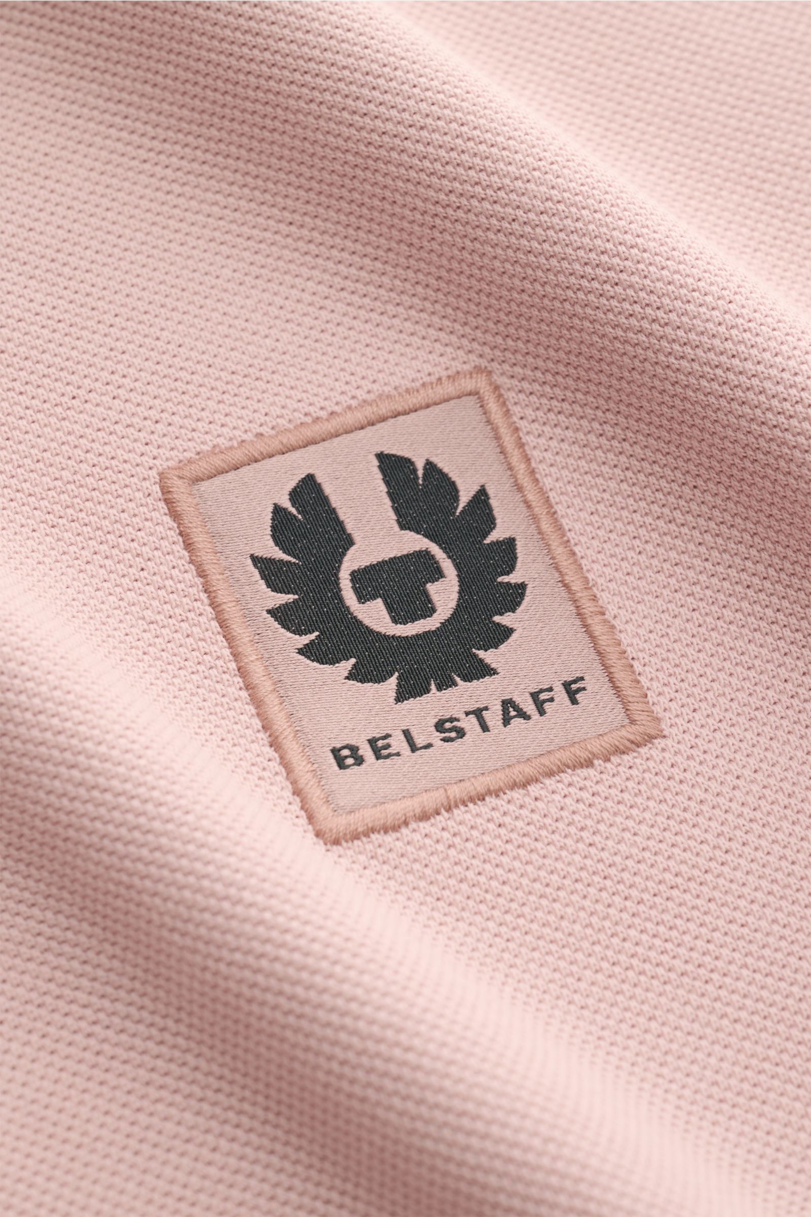 Nahaufnahme des Belstaff Poloshirts altrosa aus Piqué-Baumwolle mit leicht strukturiertem Griff und BELSTAFF-Weblabel auf der Brust.