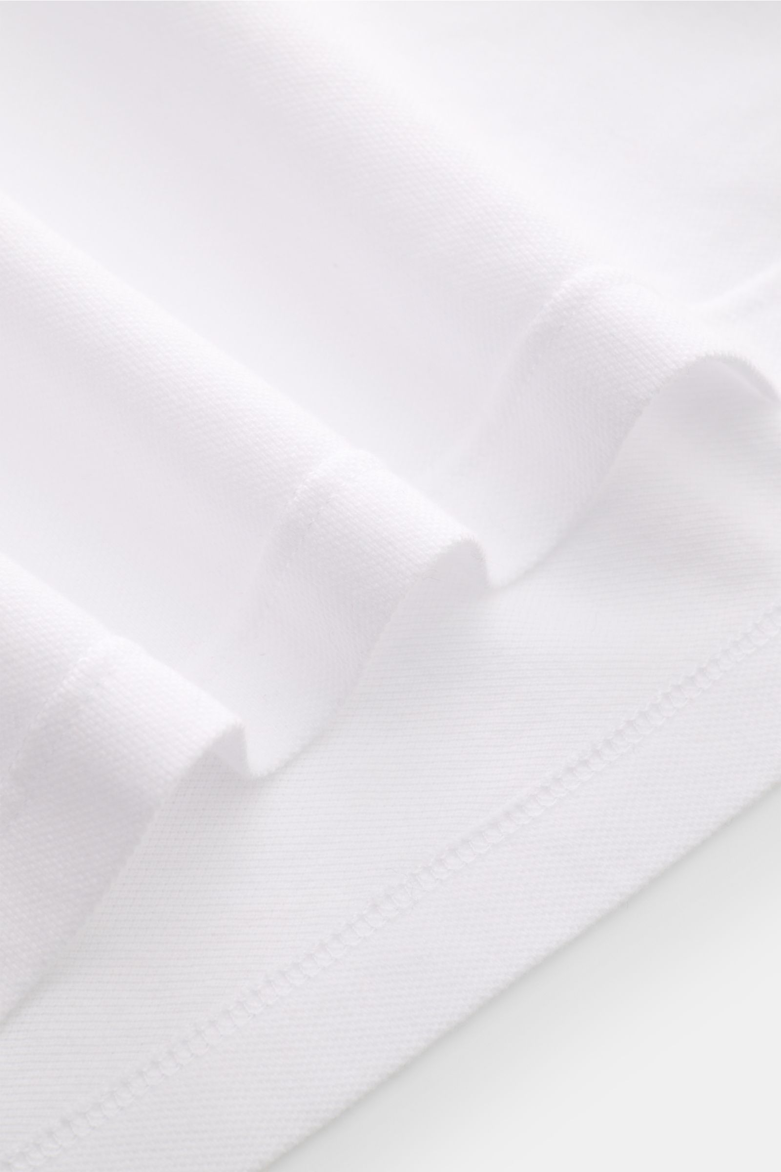 Nahaufnahme des weißen Fedeli Poloshirts 'North' aus Baumwoll-Piqué, Slim Fit, garment dyed, mit typischem Polokragen und Saumschlitzen.
