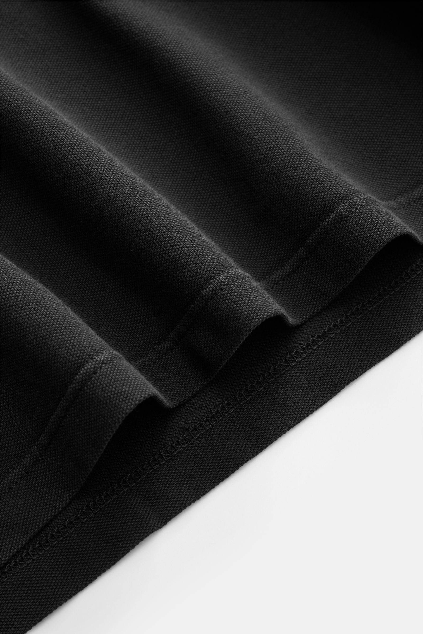Fedeli Poloshirt 'North' schwarz, Nahaufnahme des schwarzen Baumwoll-Piqué-Stoffs mit Saum, seitliche Schlitze, weicher Griff, garment dyed.